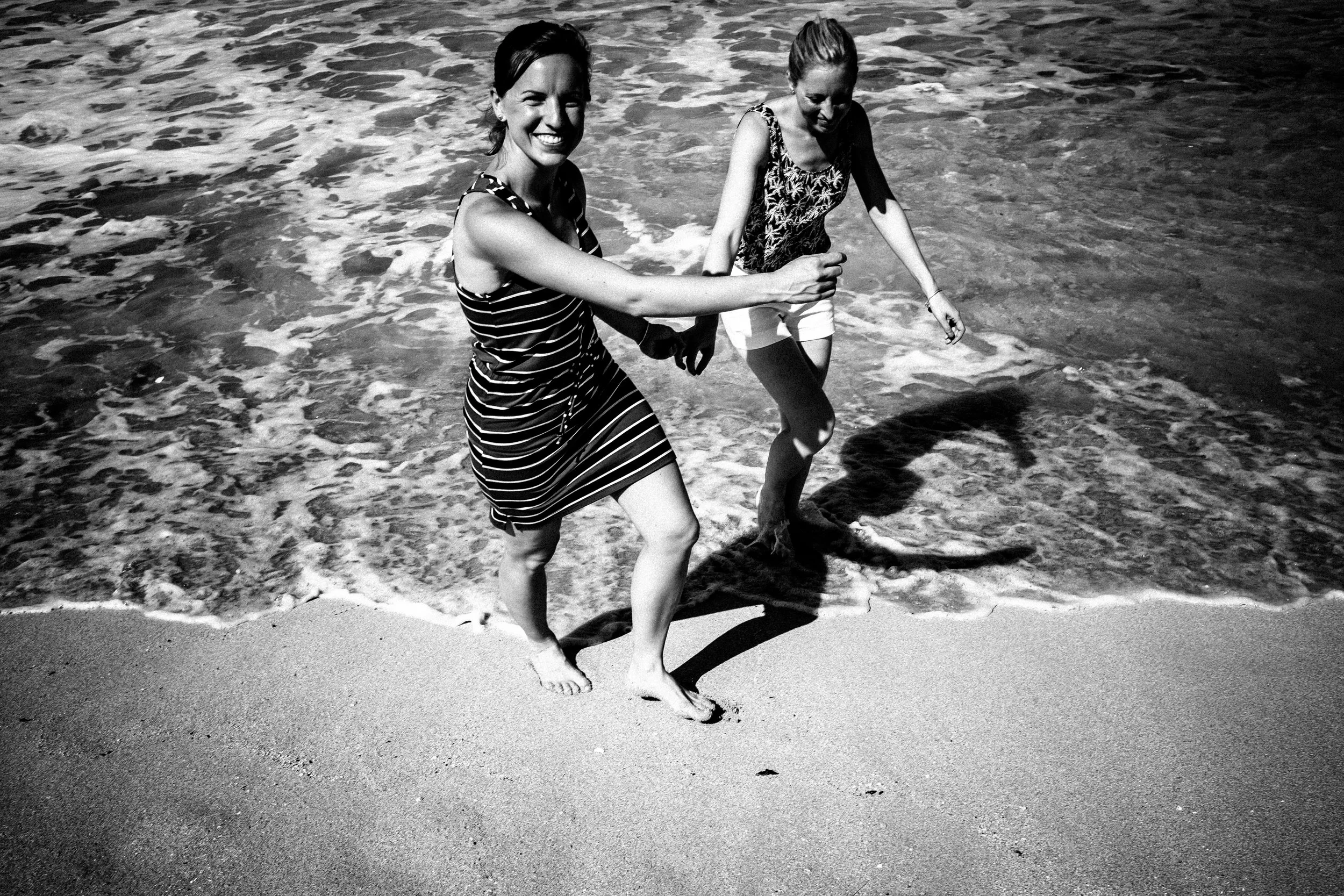 Couple laughing and running through ocean waves in black and white.