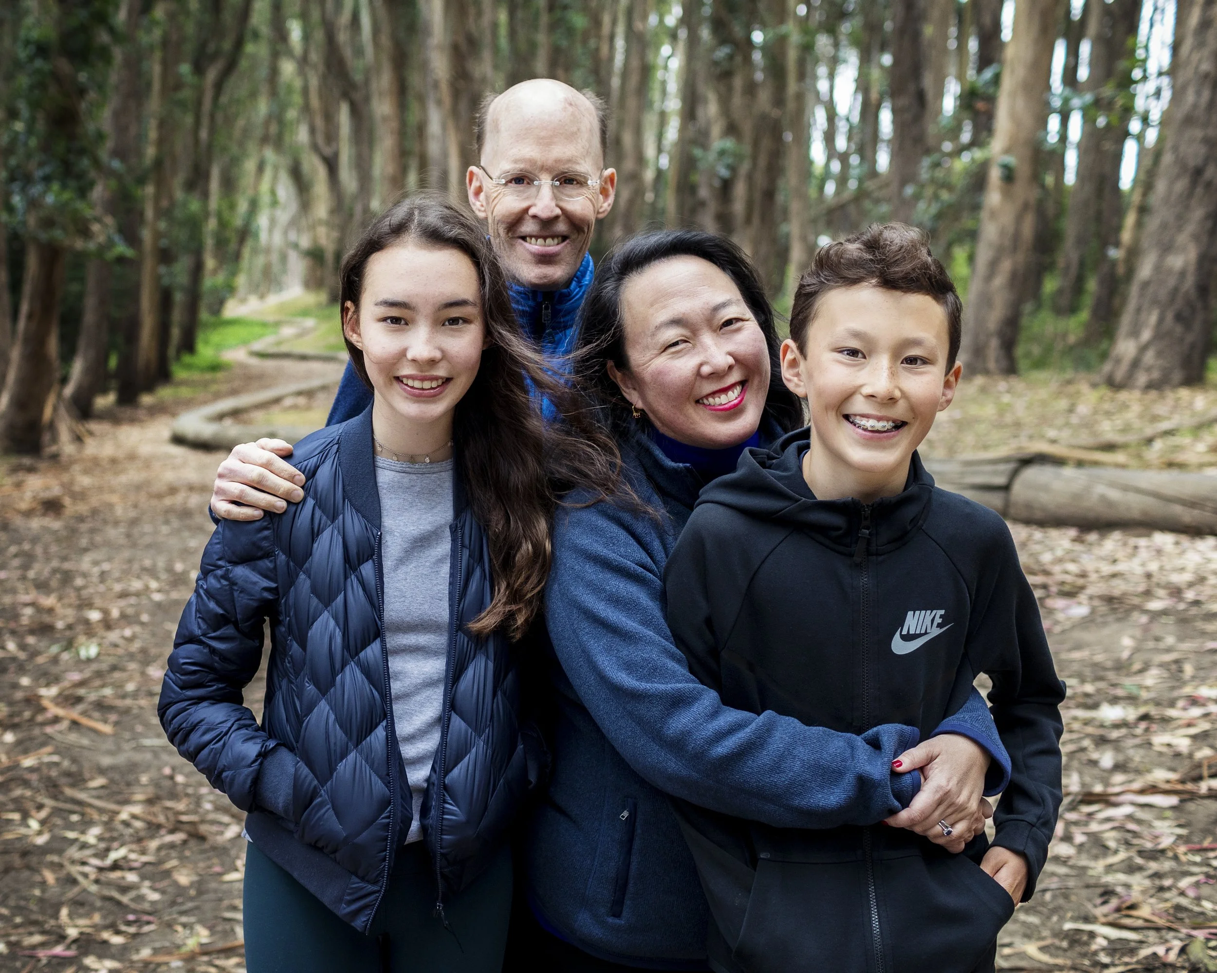 Family of four smiling together in a redwood forest.