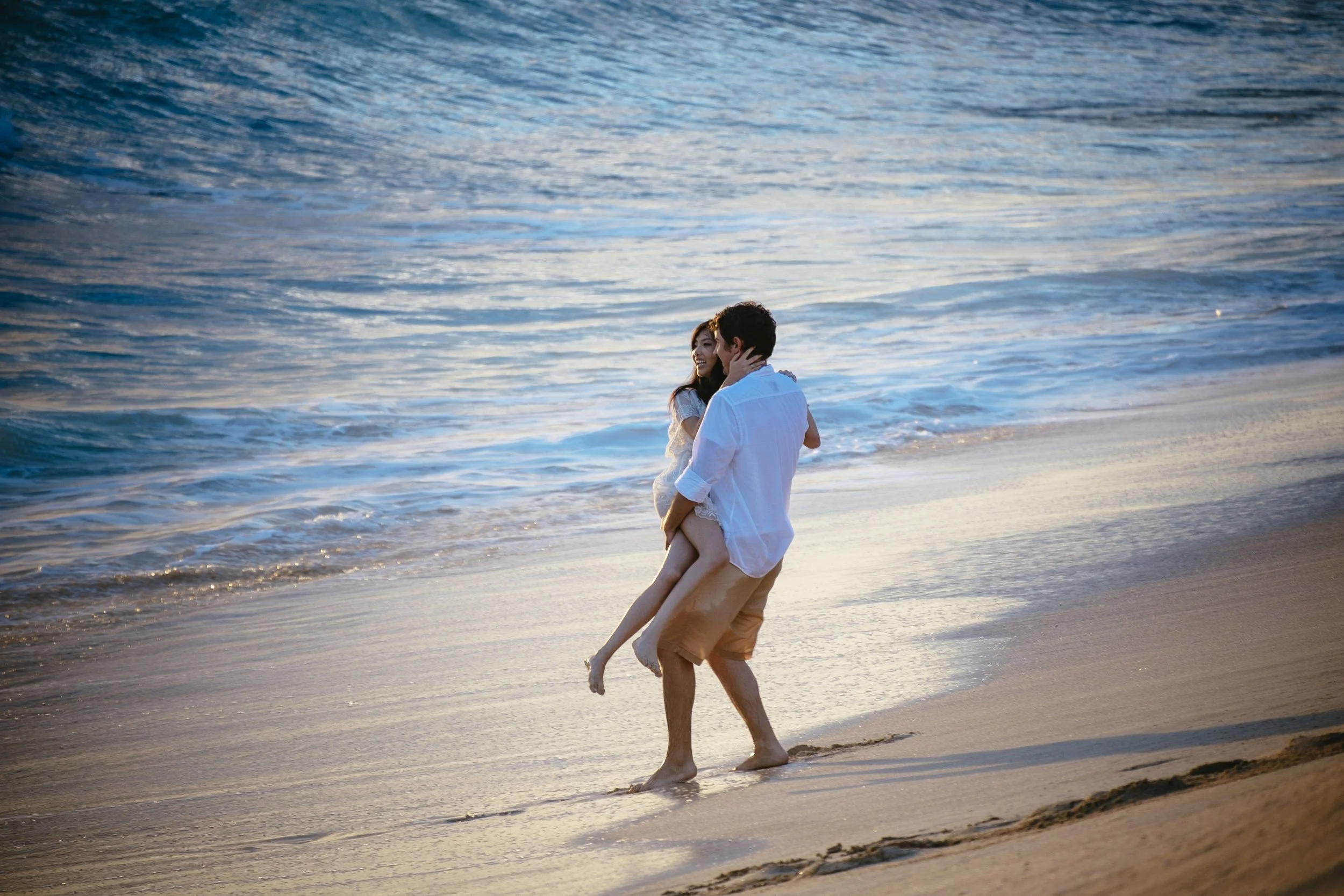 Couple embracing on a wide beach beside the blue ocean.