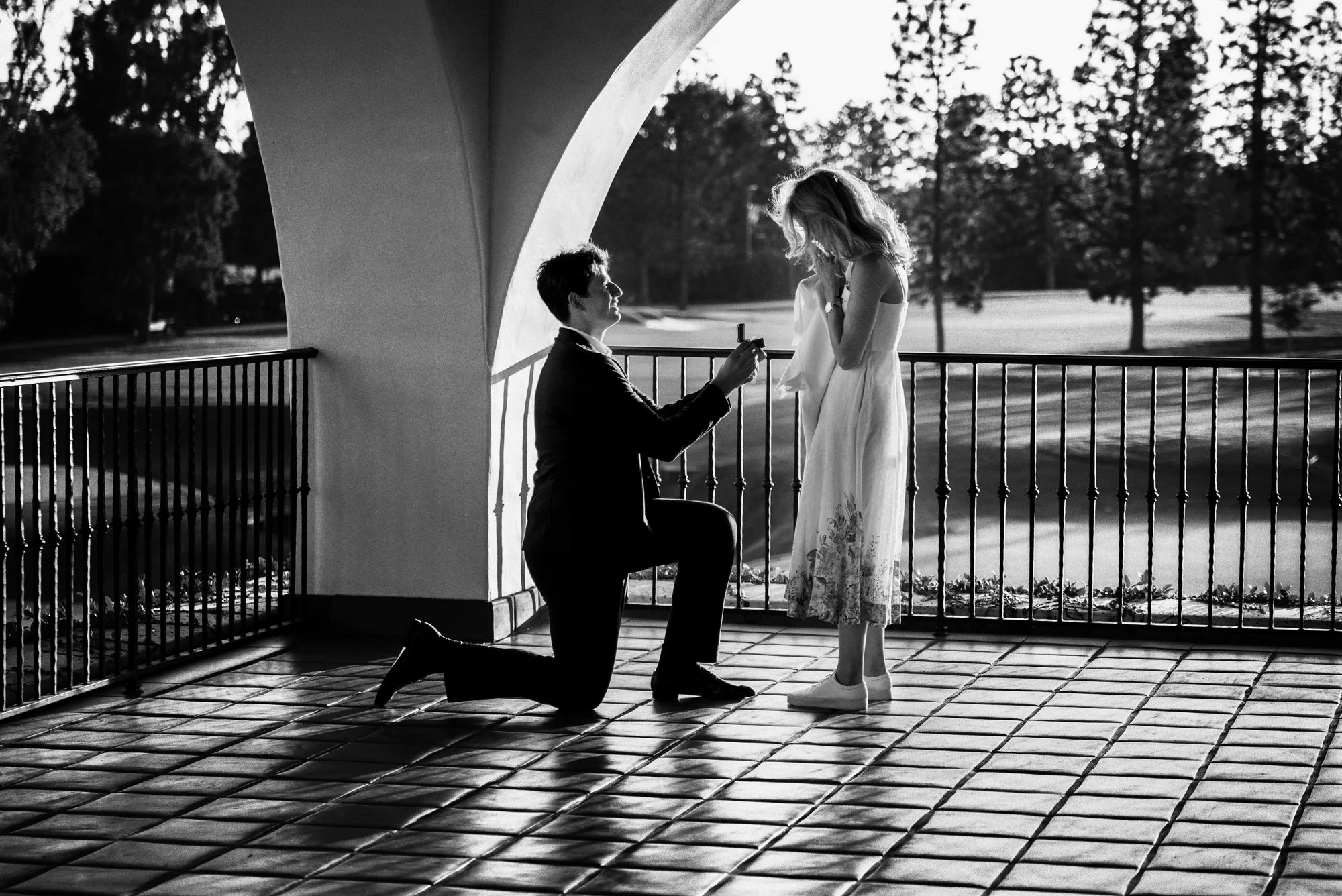 A man proposing beneath an arch at Wilshire Country Club in Los Angeles, photographed in black and white.