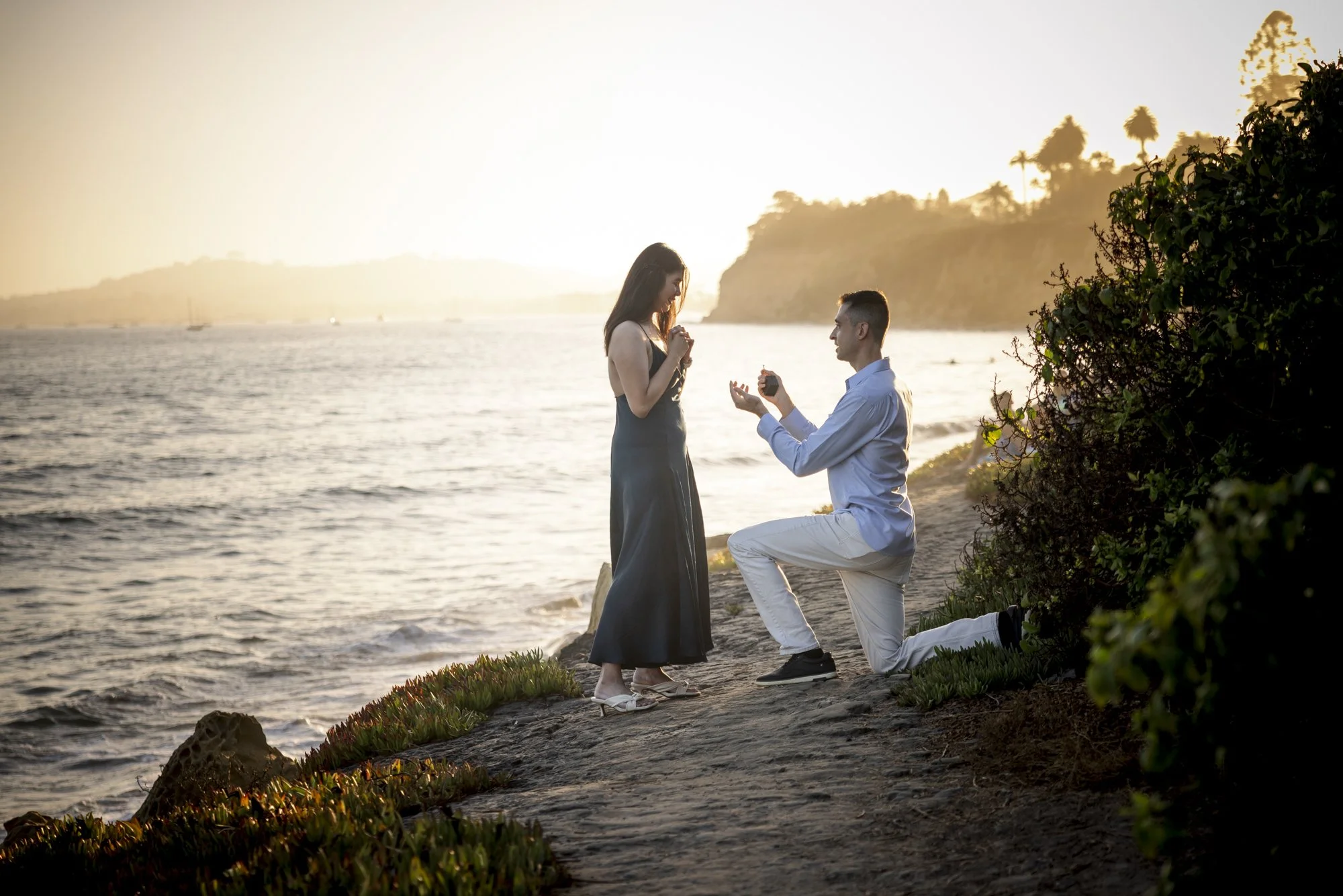 A man proposing to his girlfriend during a surprise marriage proposal at Butterfly Beach in Montecito, California at sunset.