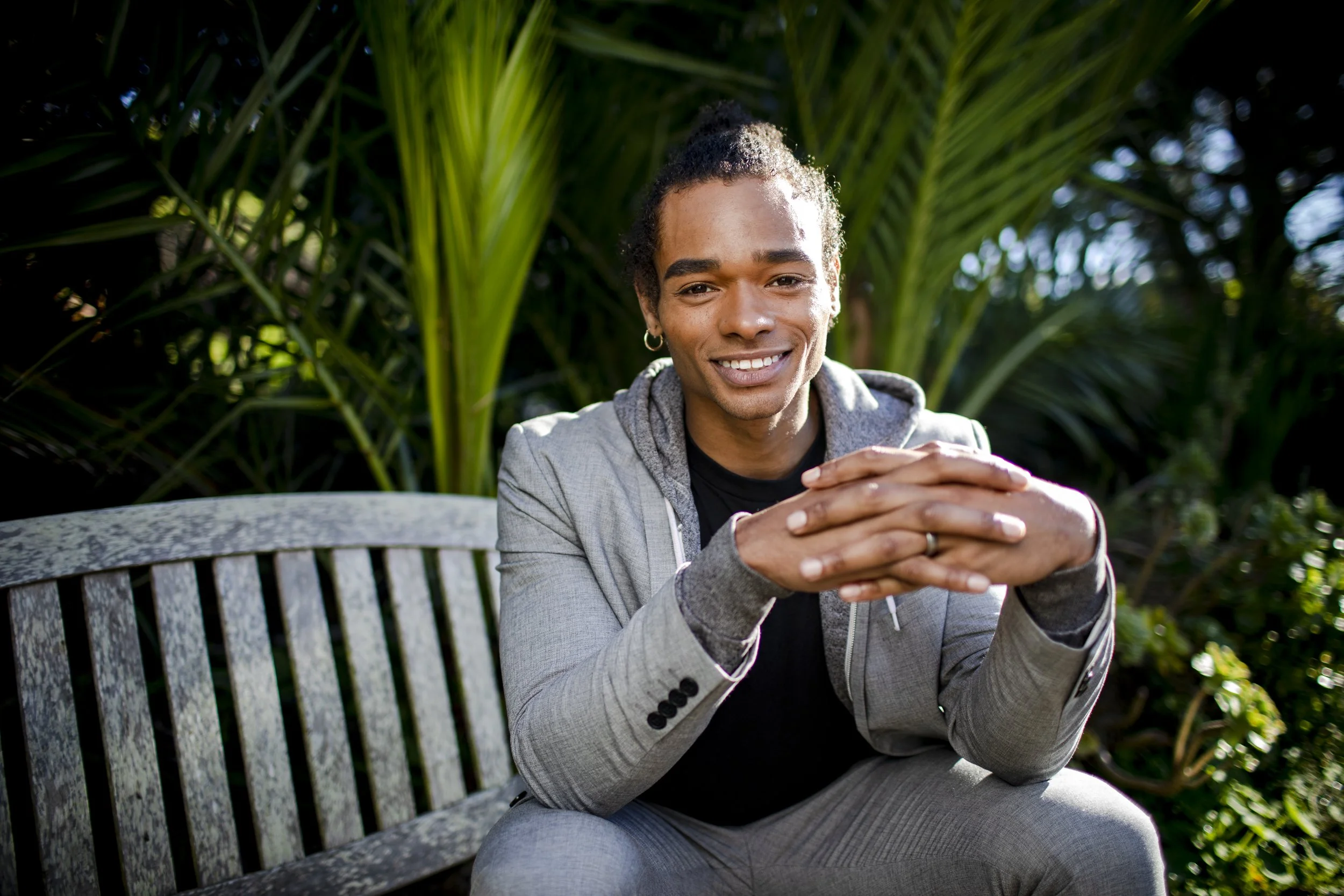 Professional seated outdoors with hands folded for a relaxed portrait.