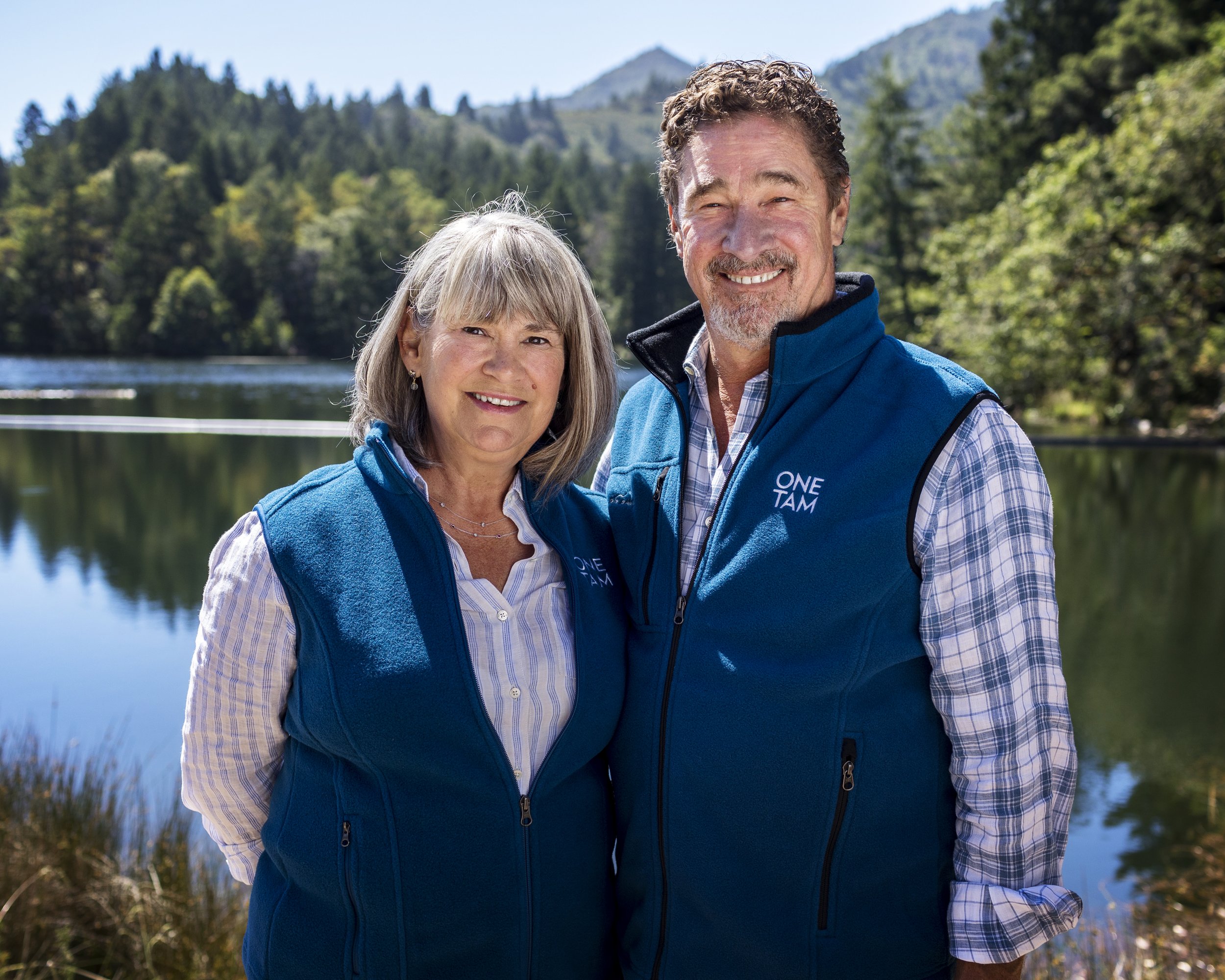 Couple smiling together beside a mountain lake.