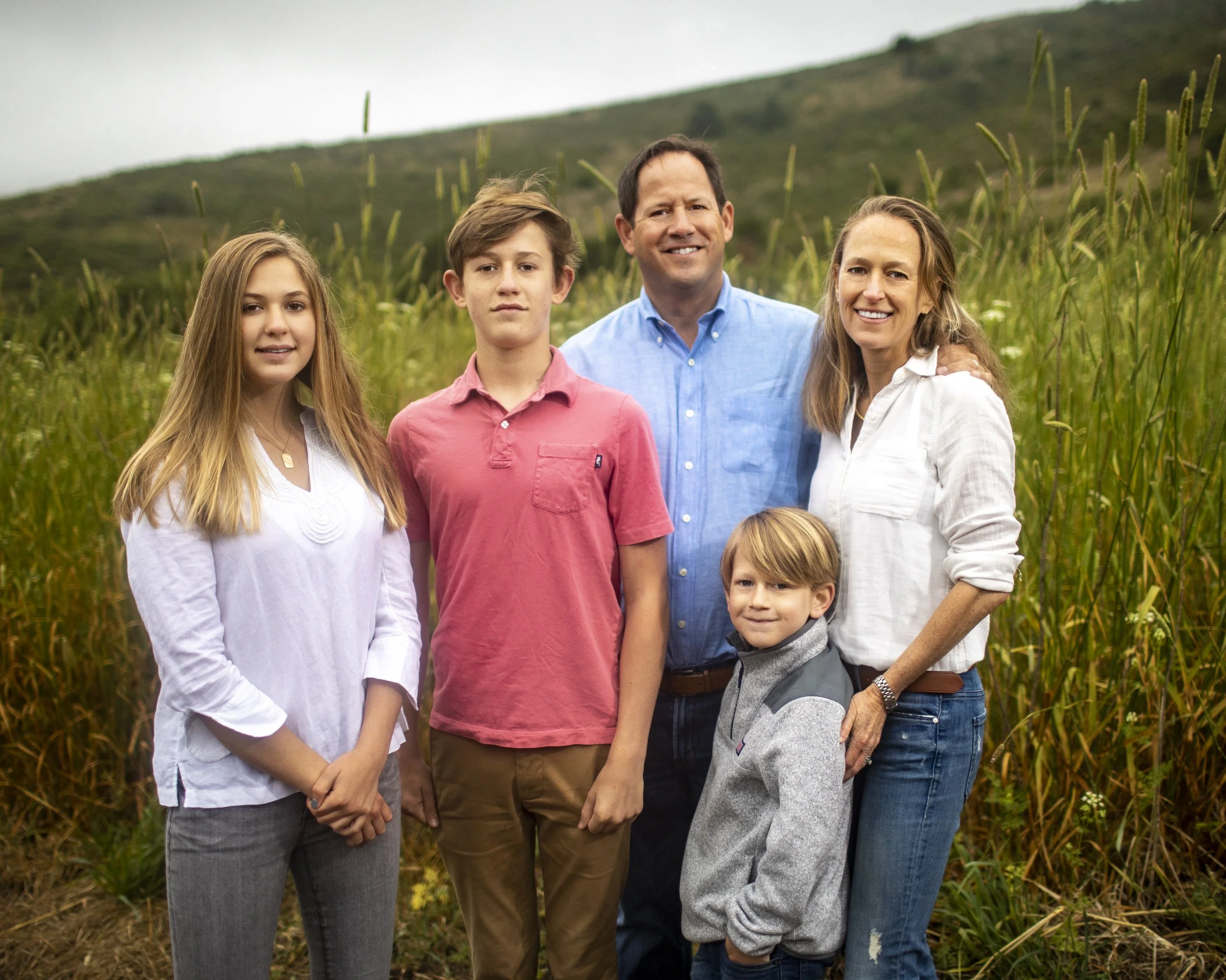 Family of five standing together in coastal hills.