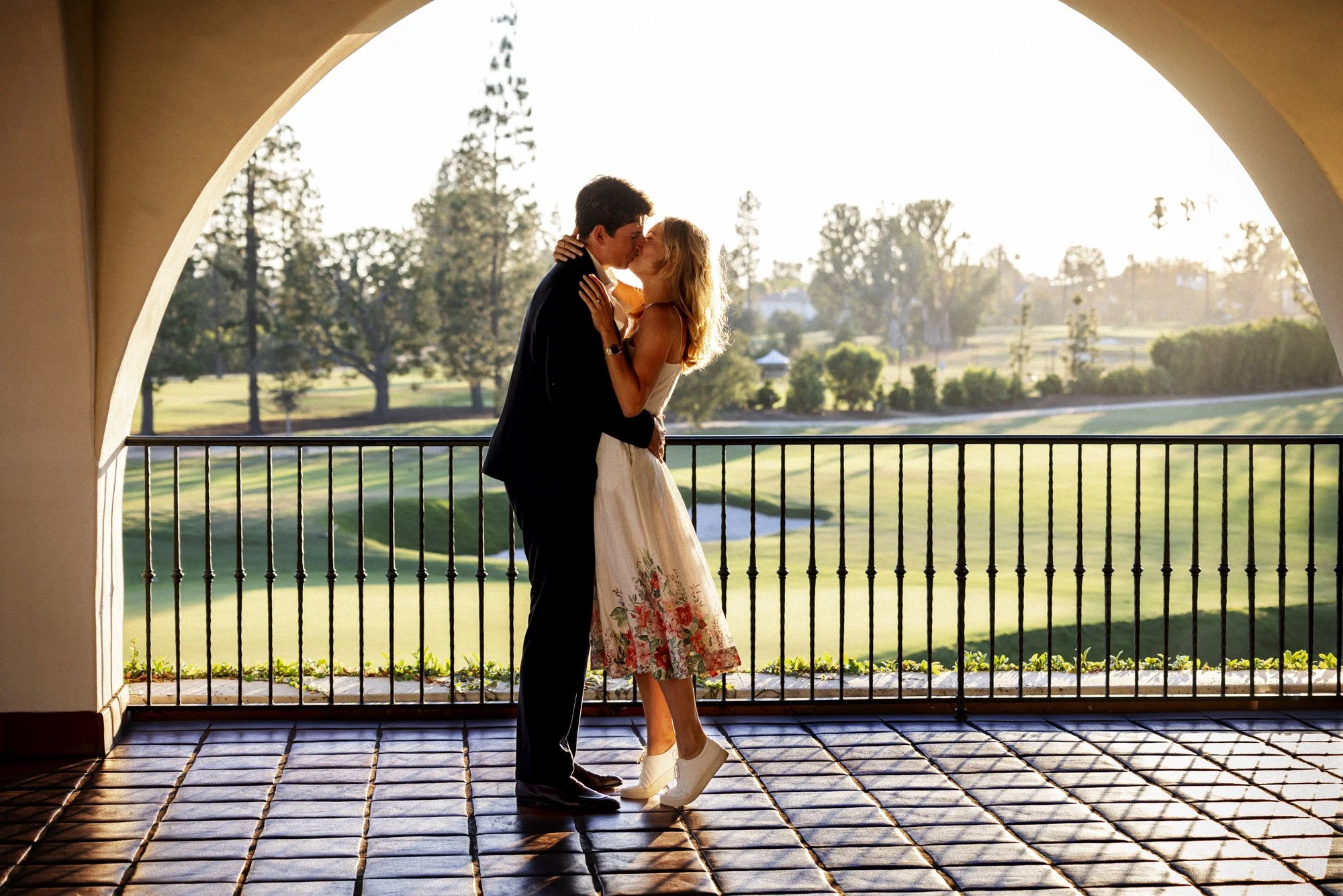 Newly engaged couple kissing beneath an arch in warm evening light at Wilshire Country Club in Los Angeles.