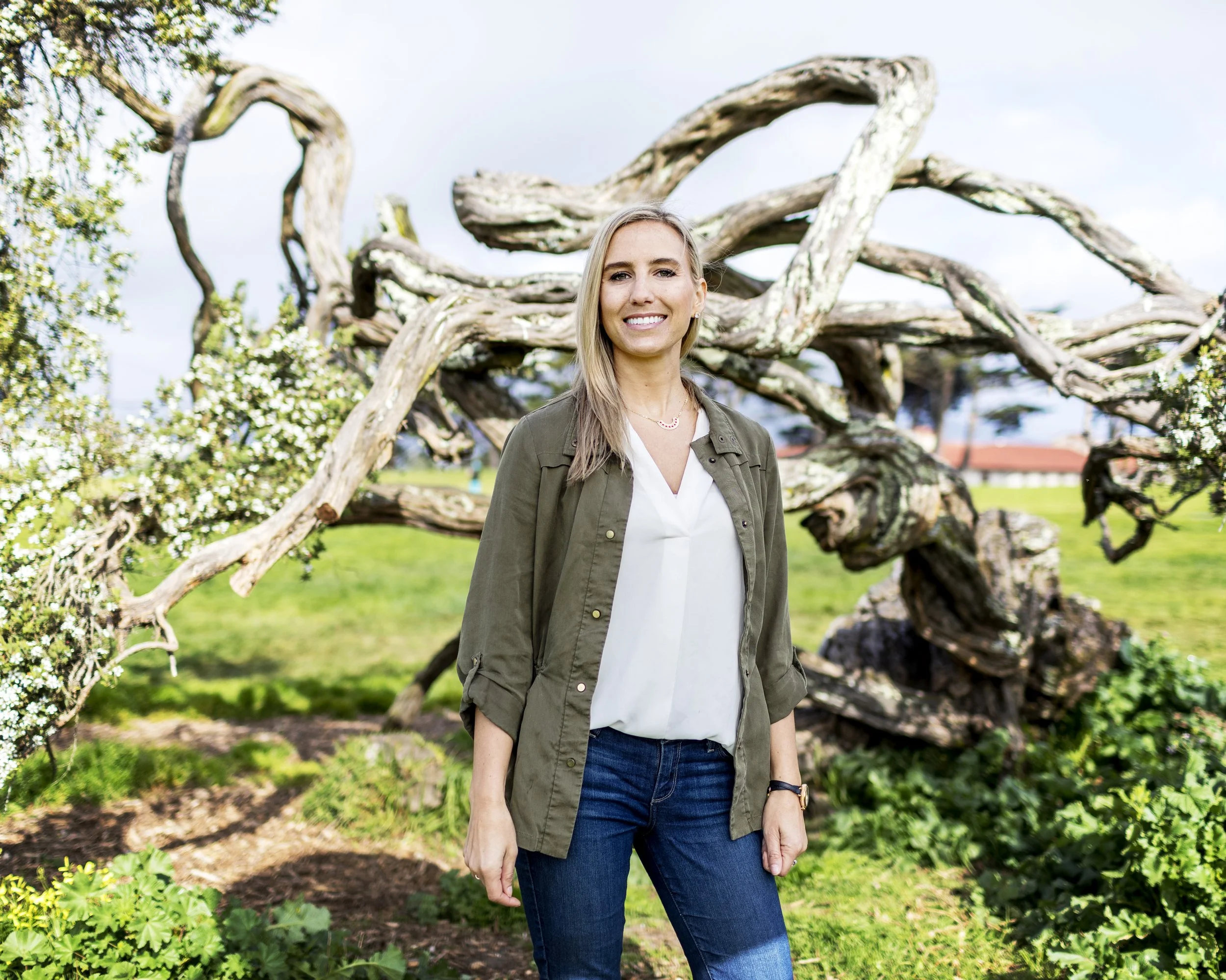 Woman standing beside sculptural tree branches in an outdoor portrait.
