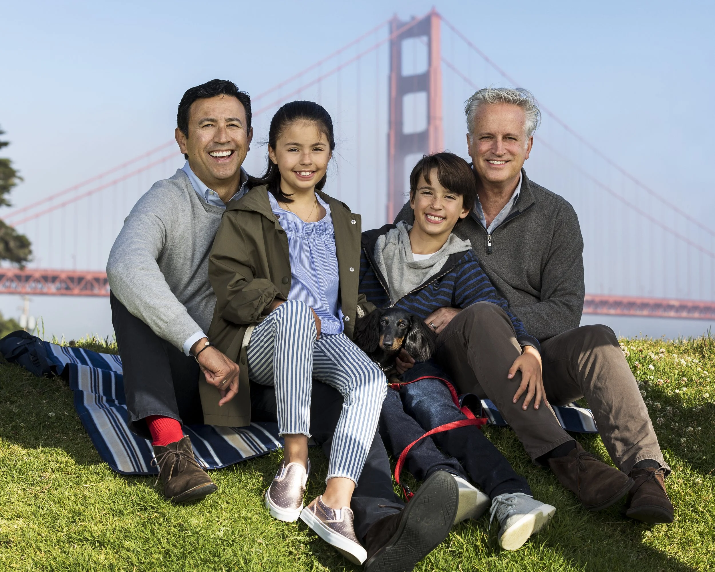 Family of four seated together with the Golden Gate Bridge behind them.