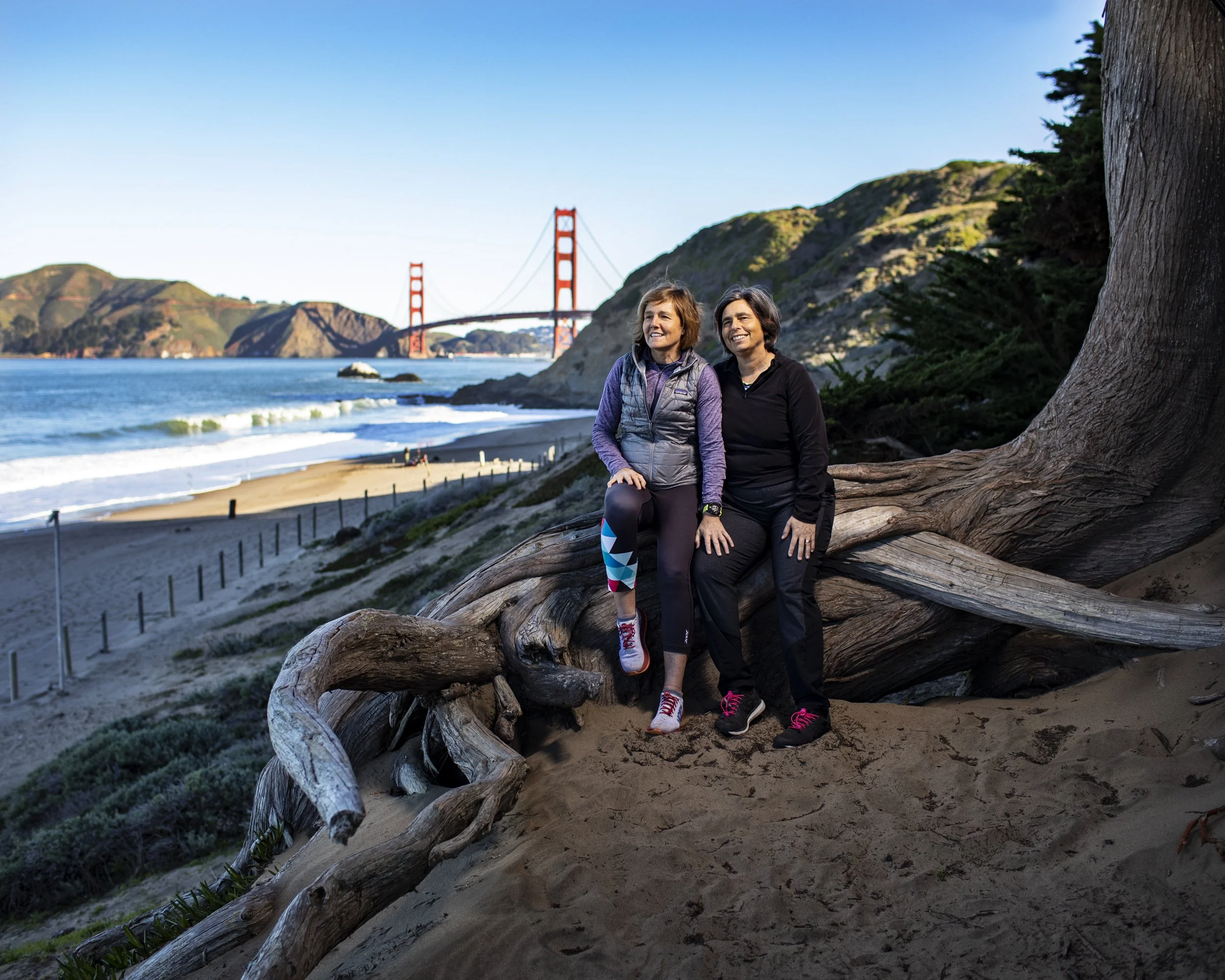 Couple sitting on a log on a beach near the Golden Gate Bridge.