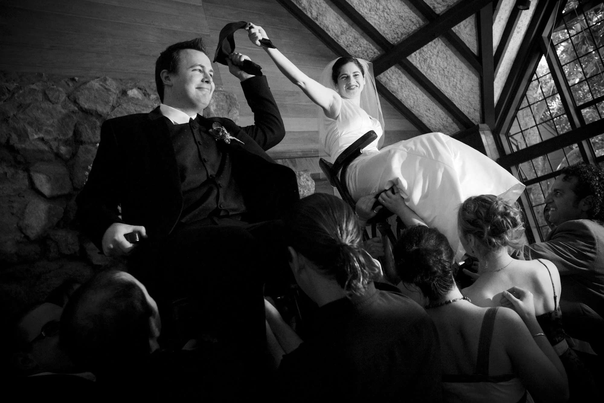 Bride and groom lifted above guests during an exuberant wedding dance.