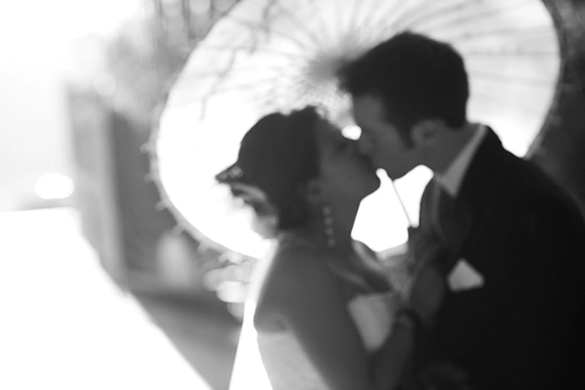 Silhouetted newlyweds touching foreheads in a bright circular window.