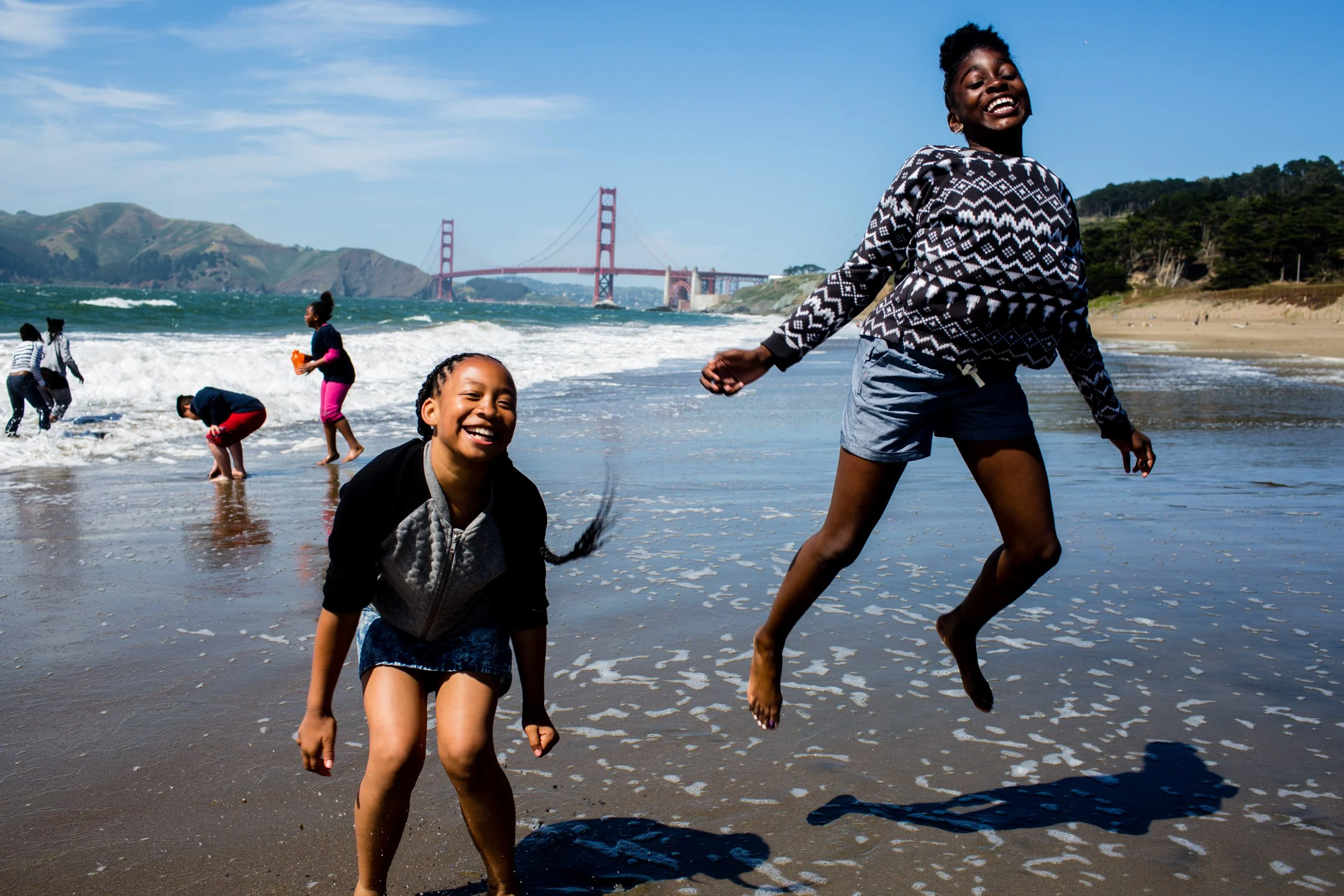 Children jumping and playing on a beach with the Golden Gate Bridge behind them.