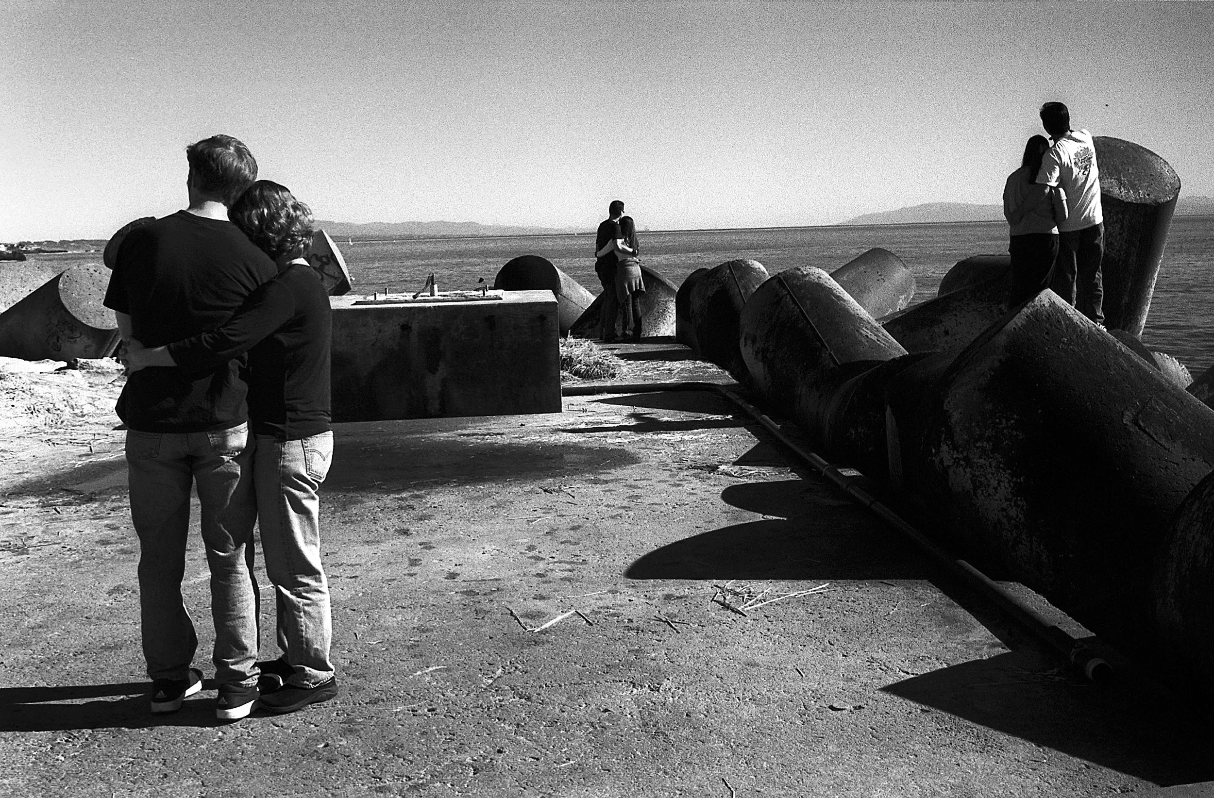 Couple standing together on a breakwater in Santa Cruz in black and white.