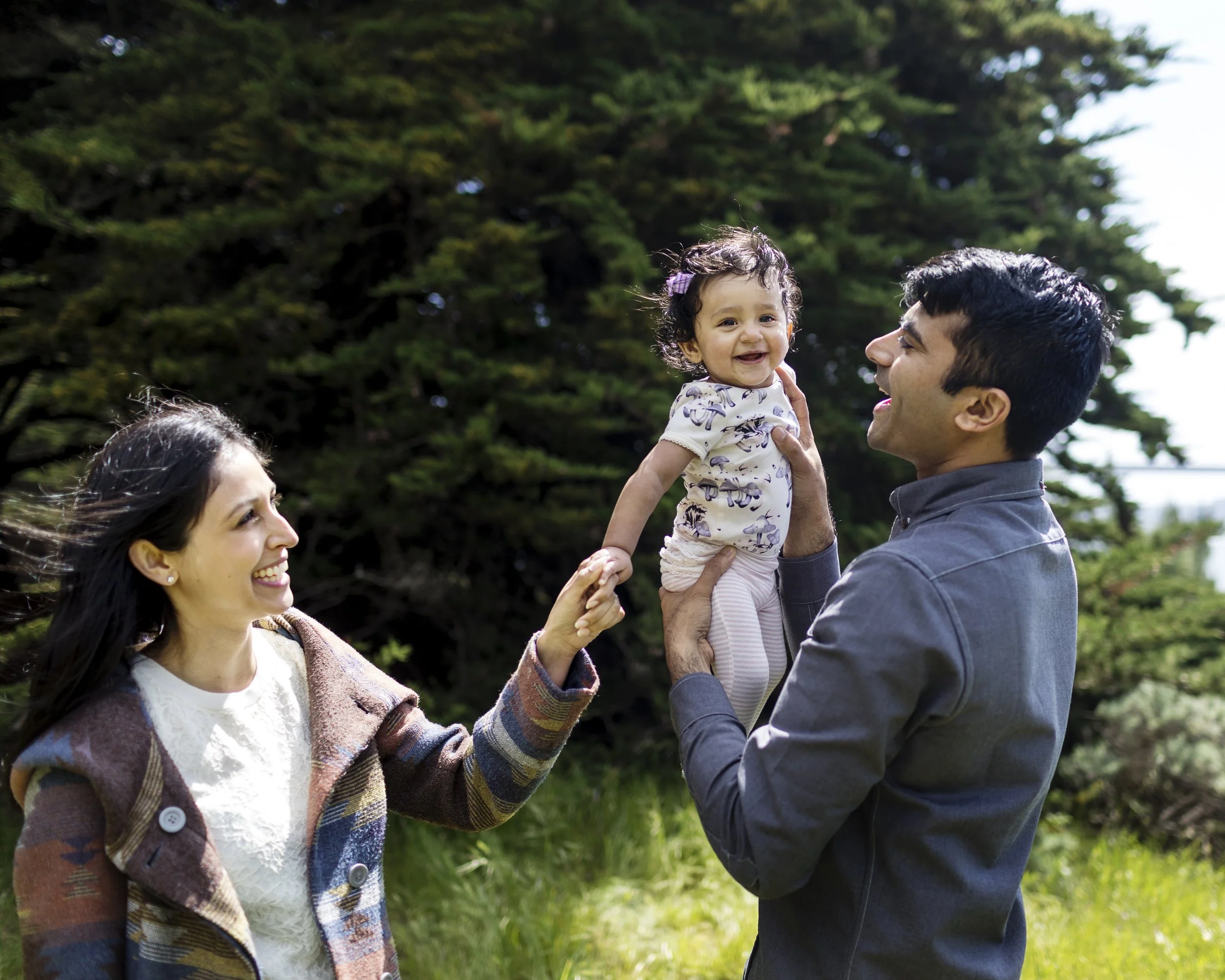 Parents smiling and playing with their toddler during an outdoor family session.