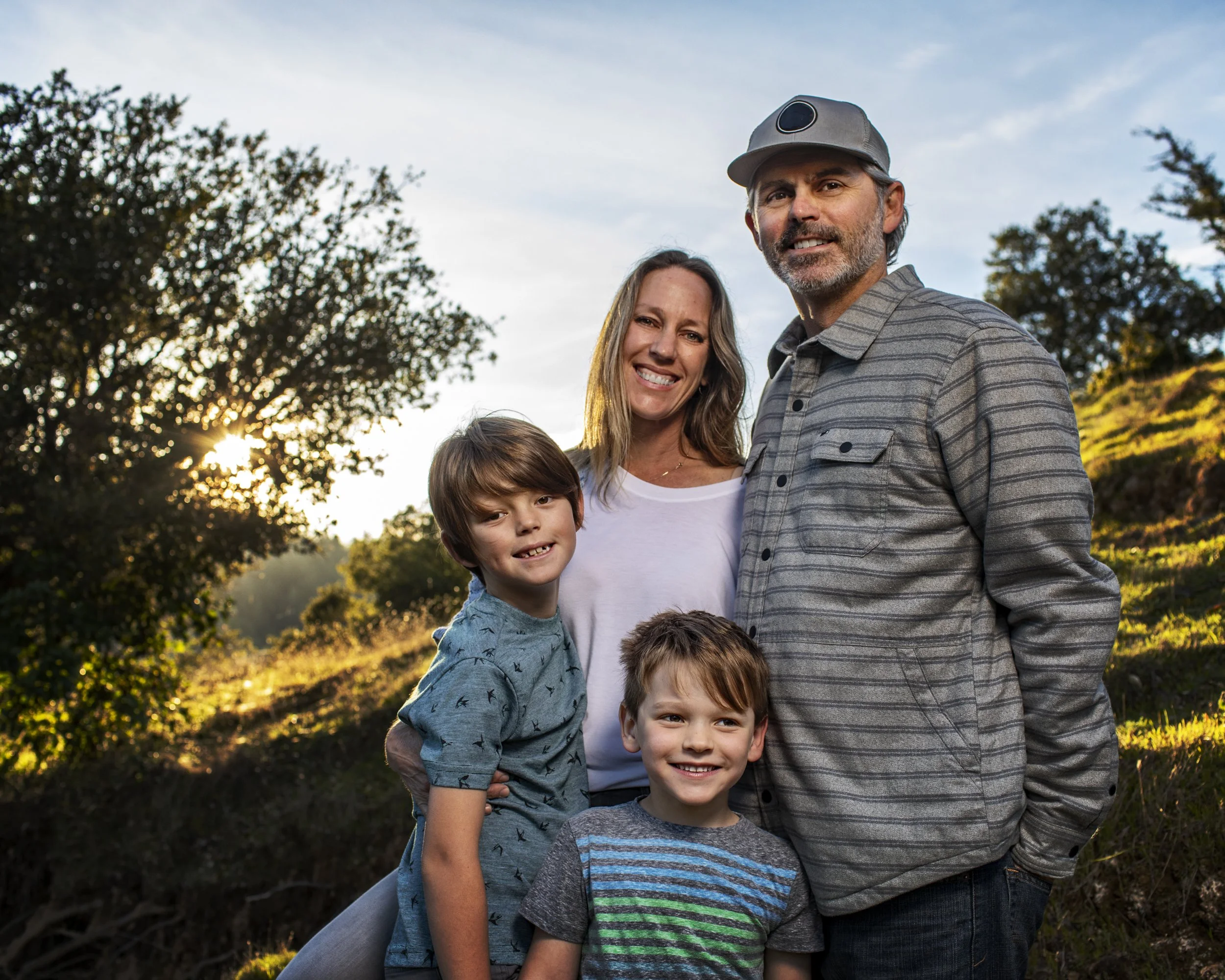 Family of four standing together in warm sunset light.