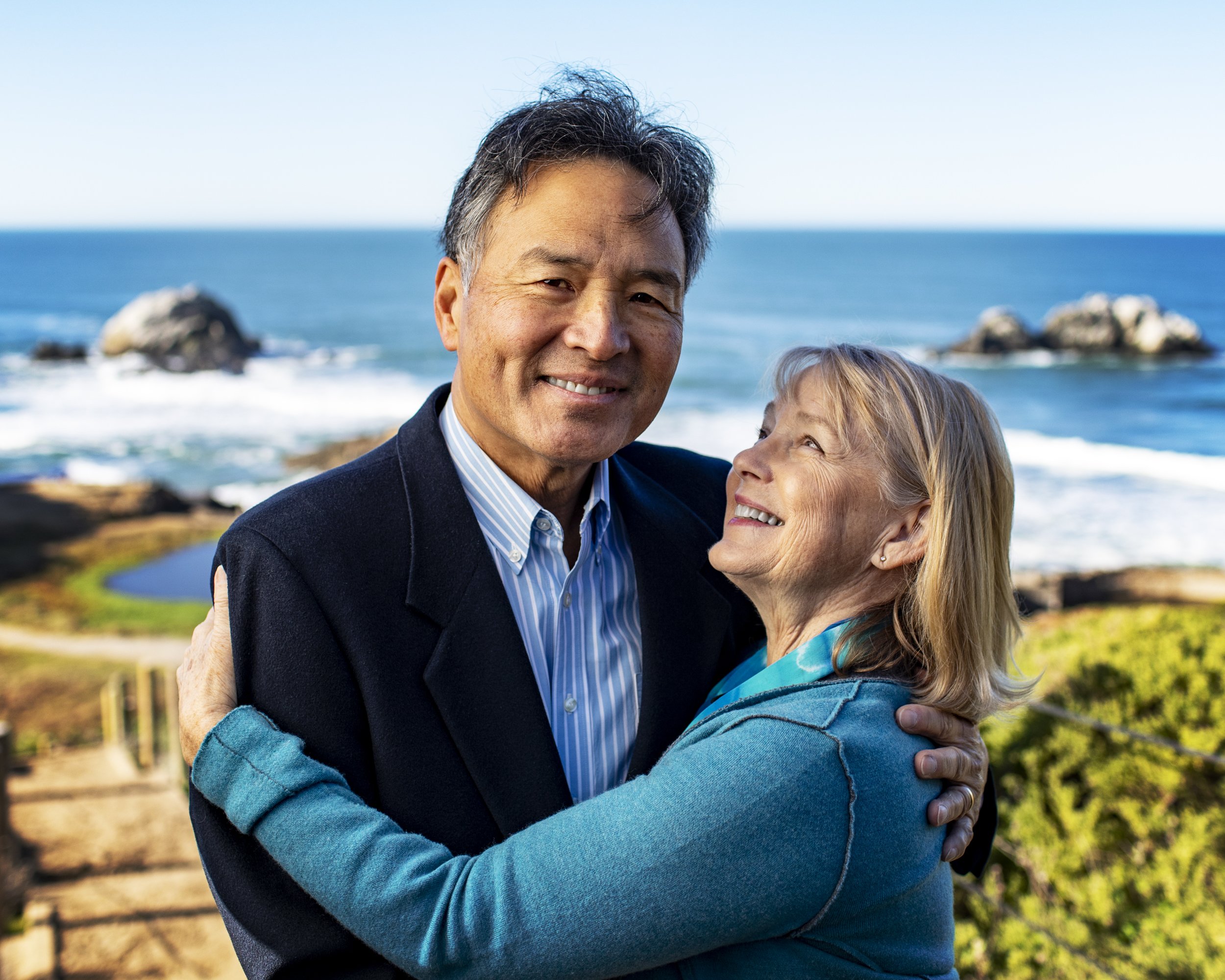 Older couple smiling and holding each other beside the California coast.