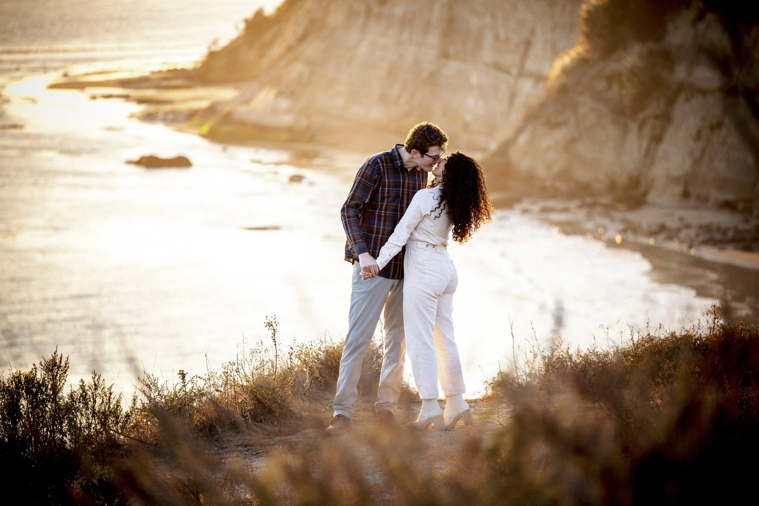 Newly engaged couple kissing above the Santa Barbara shoreline at golden hour.