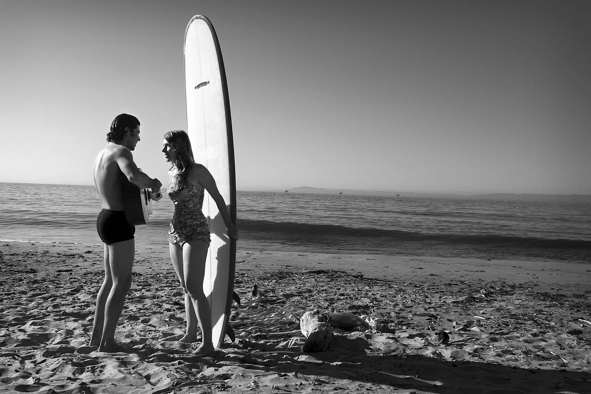 Couple standing face to face beside a surfboard at Miramar Beach in Montecito.