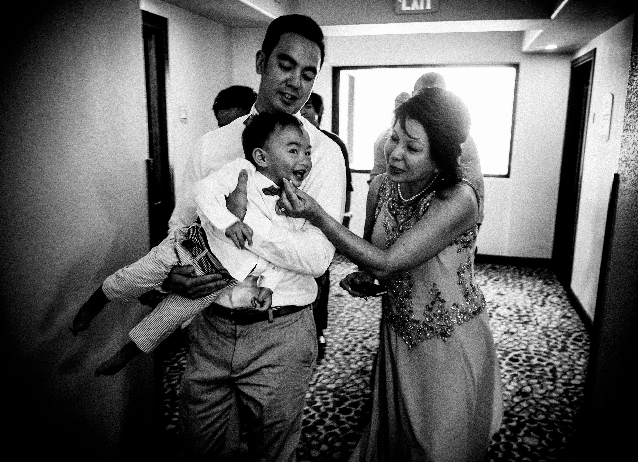 Wedding party laughing and embracing in a hotel hallway.