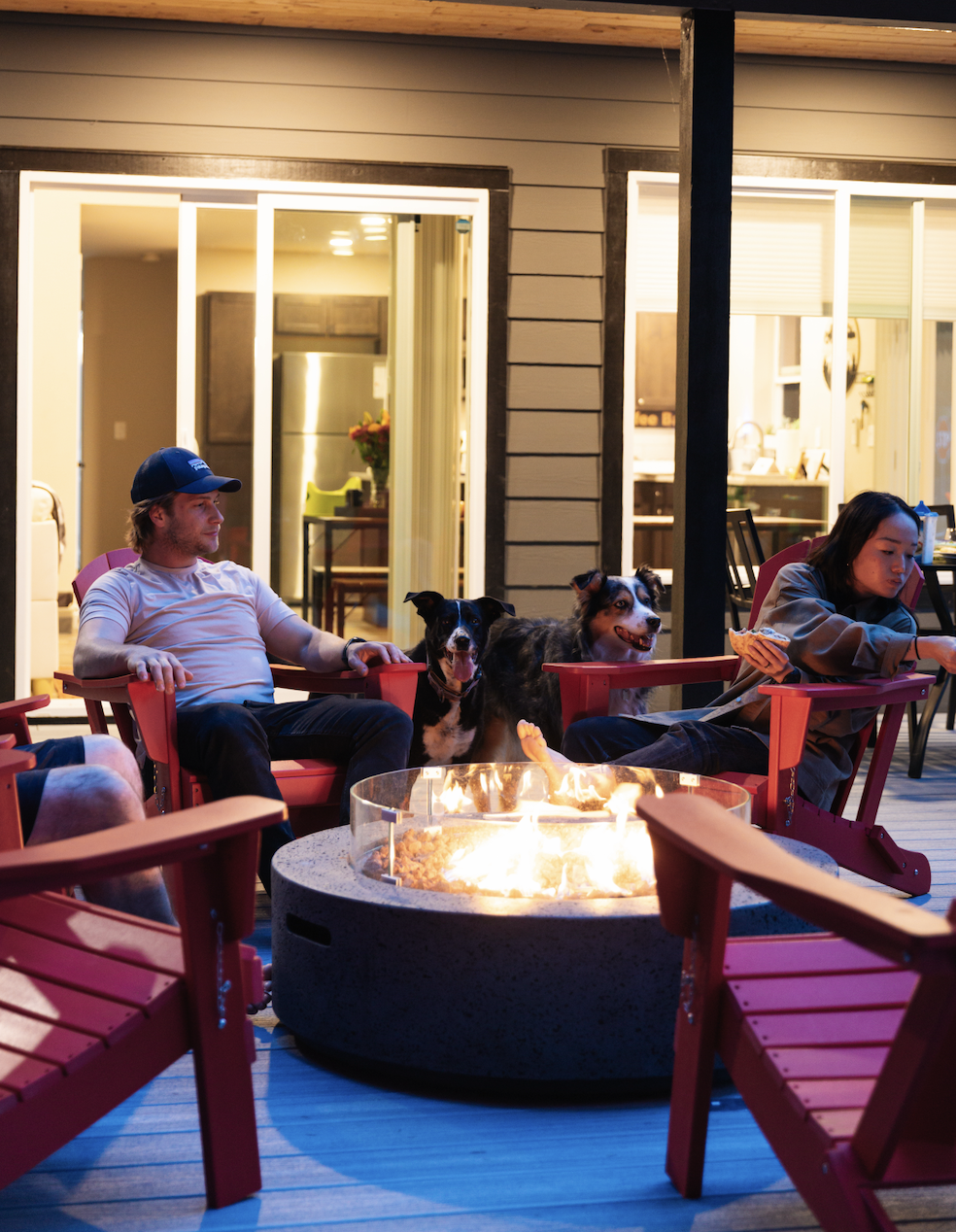 Couple and dogs sitting by the fire pit outside of their cabin stay