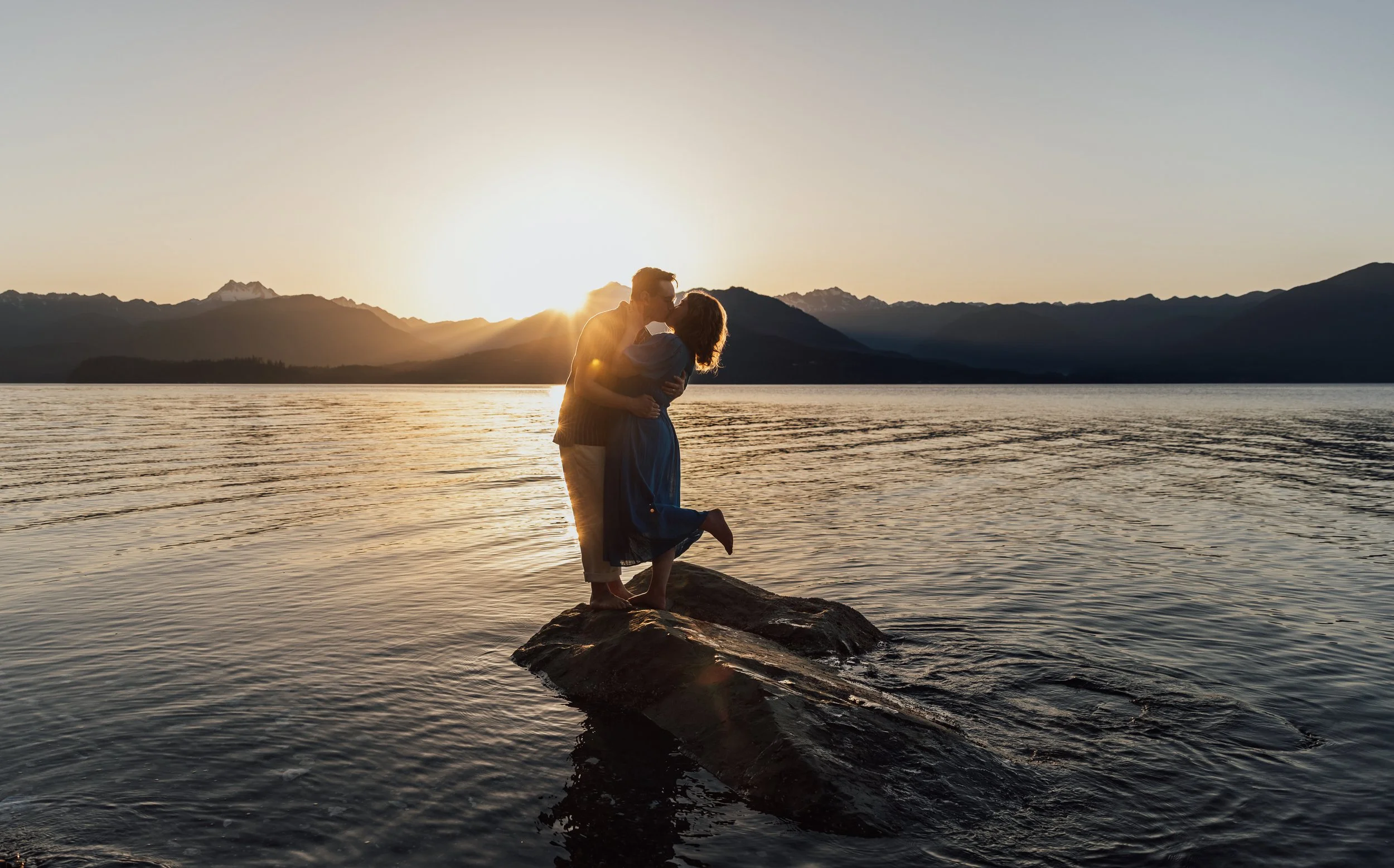 Engagement photoshoot with couple standing on a rock during sunset