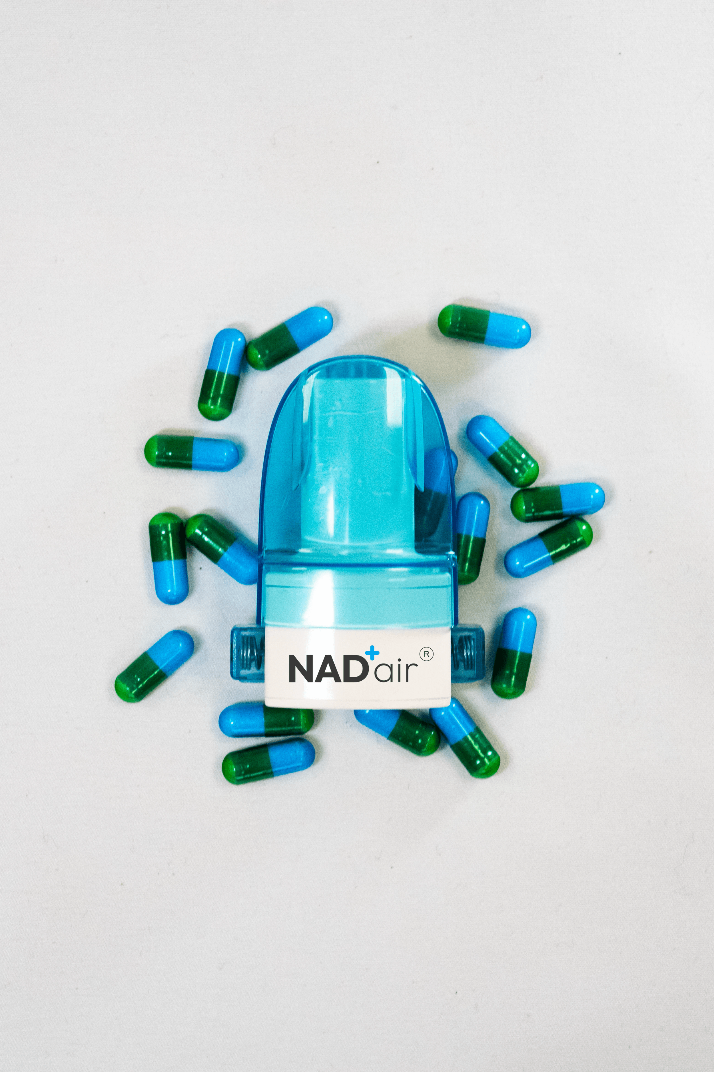 A nasal spray bottle labeled 'NAD air' surrounded by blue and green capsules on a white surface.