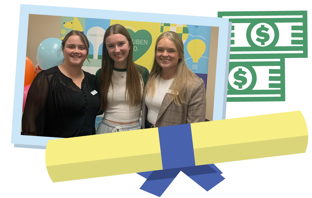Three women smiling and standing together in front of a colorful backdrop with balloons and a money-themed graphic, at an event or celebration.