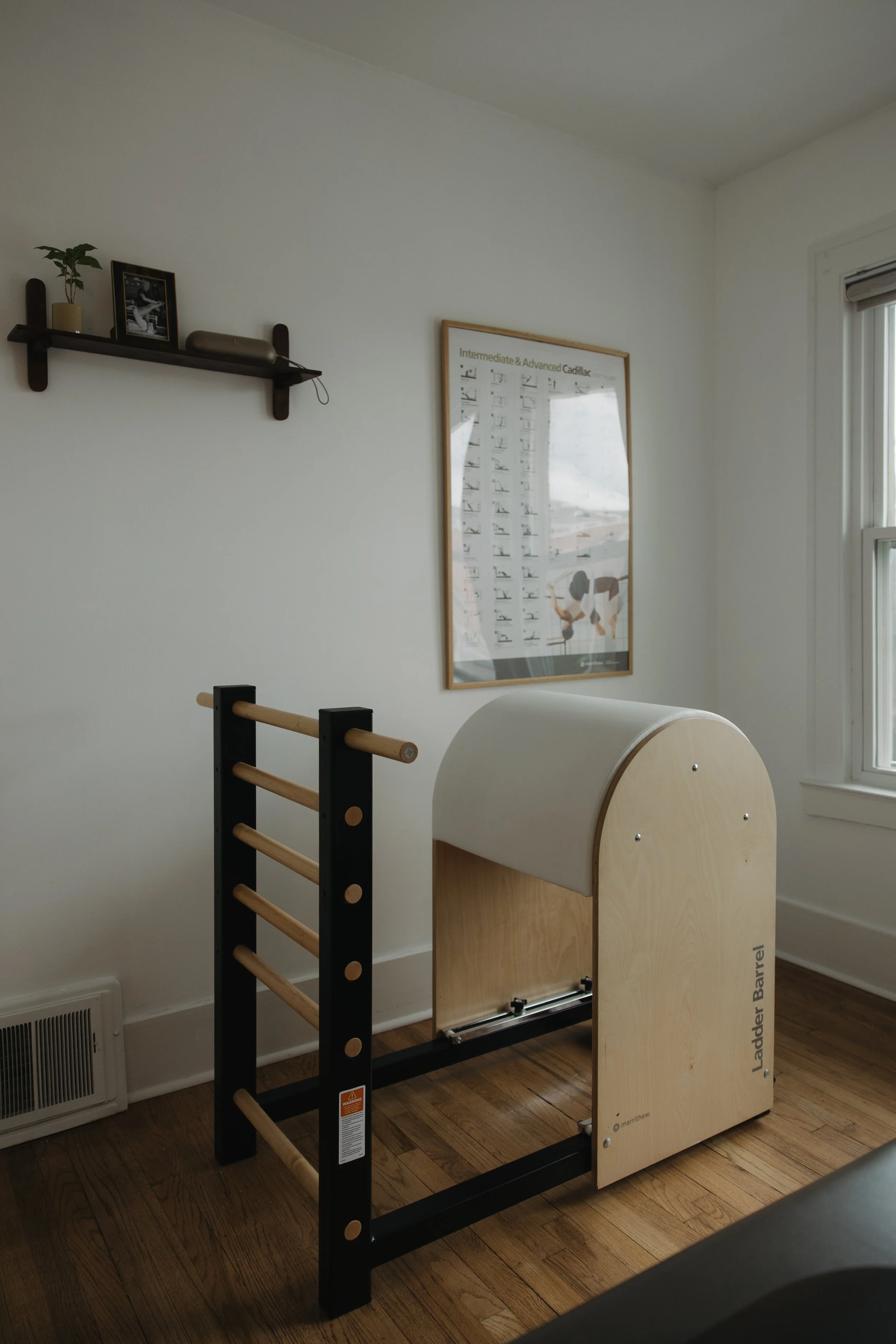 Private pilates room with a ladder barrel near a window and a framed fitness poster on the wall.