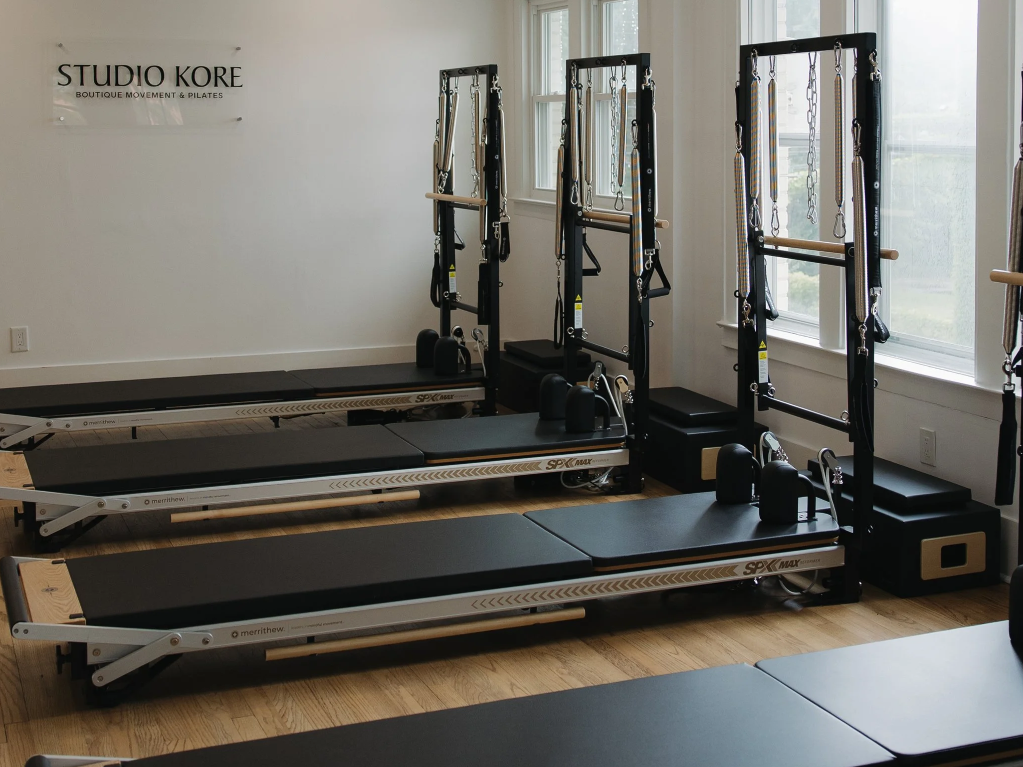 Interior of a Pilates studio with two reformer machines and a wall sign reading 'Studio Kore Boutique Movement & Pilates'.