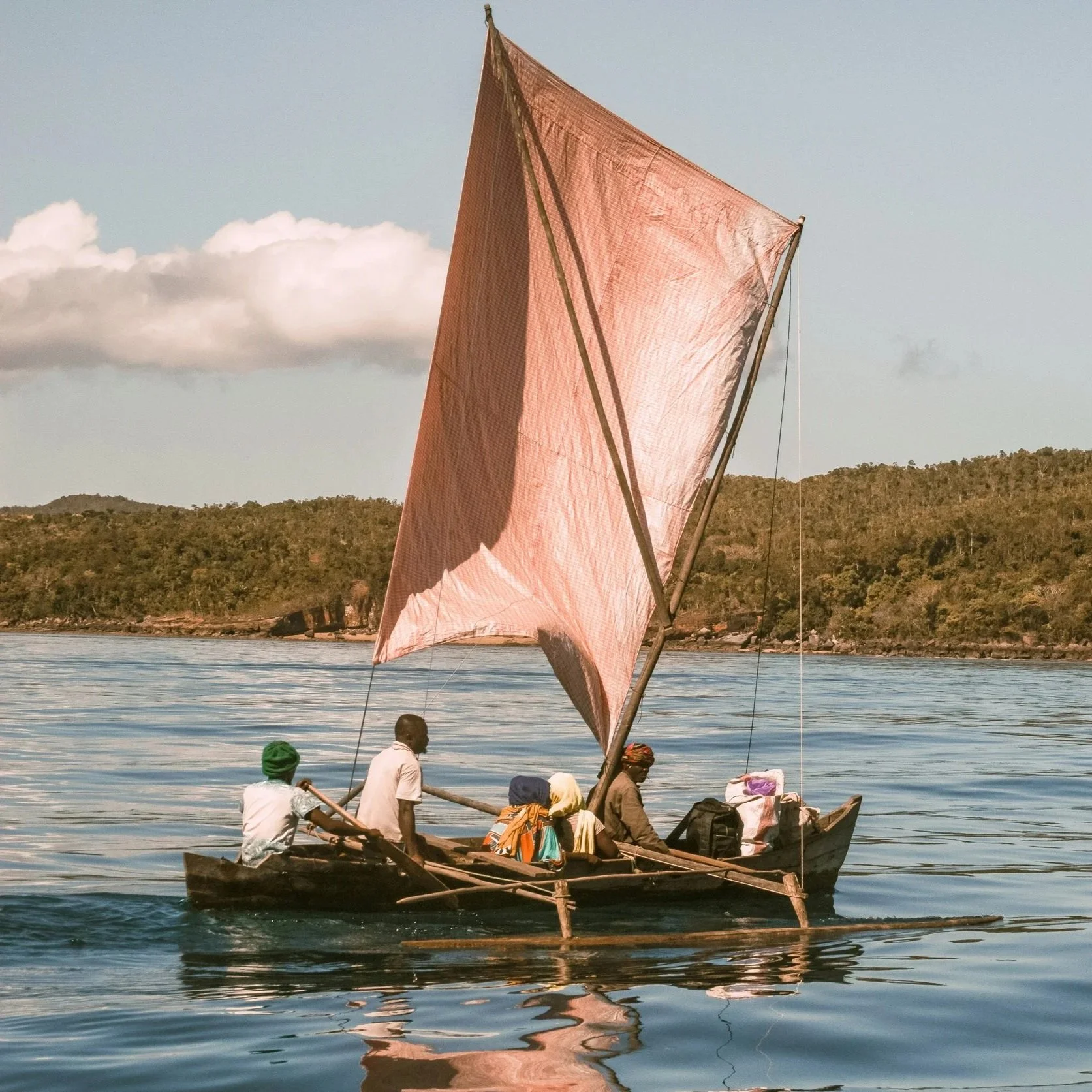 A small sailboat in the water with three people, with green hills in the background.
