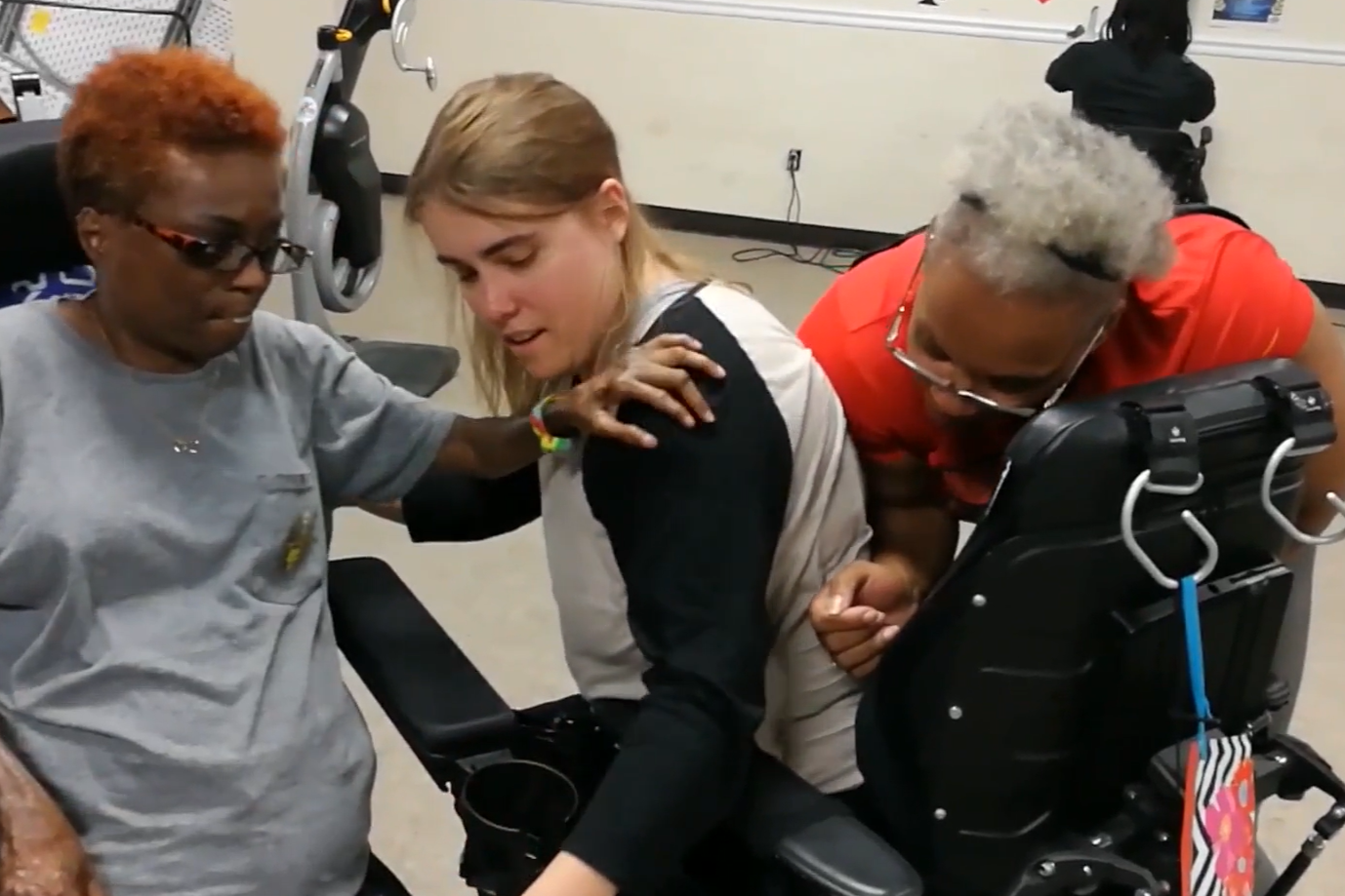 Three participants, including one in a power wheelchair, practicing a supported movement
