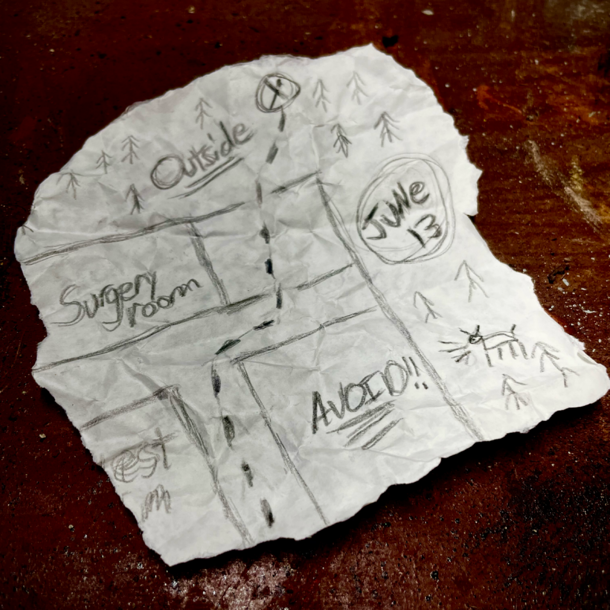 A crumpled piece of paper with a hand-drawn map, indicating directions with arrows, labels for different areas such as 'Super Room,' 'Outside,' and 'AVOID!!,' a compass, and various symbols, all sketched in pencil.
