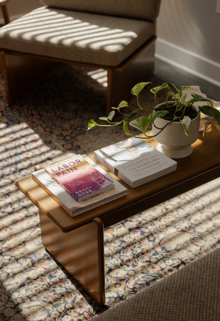 Wooden coffee table with a potted plant and three books on it, in a room with sunlight and a patterned rug.