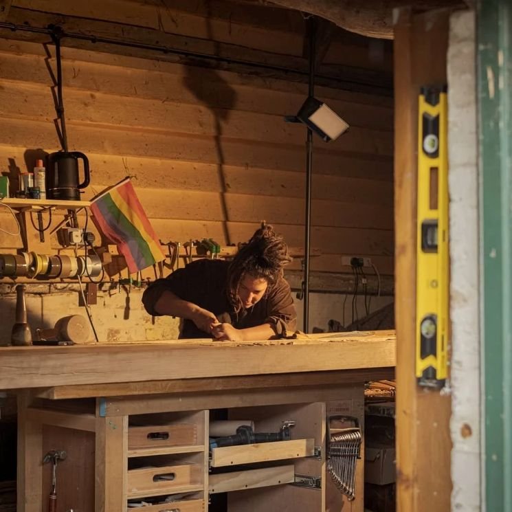 Woodcarver working inside a sunlit workshop in Southern England, viewed from an open doorway
