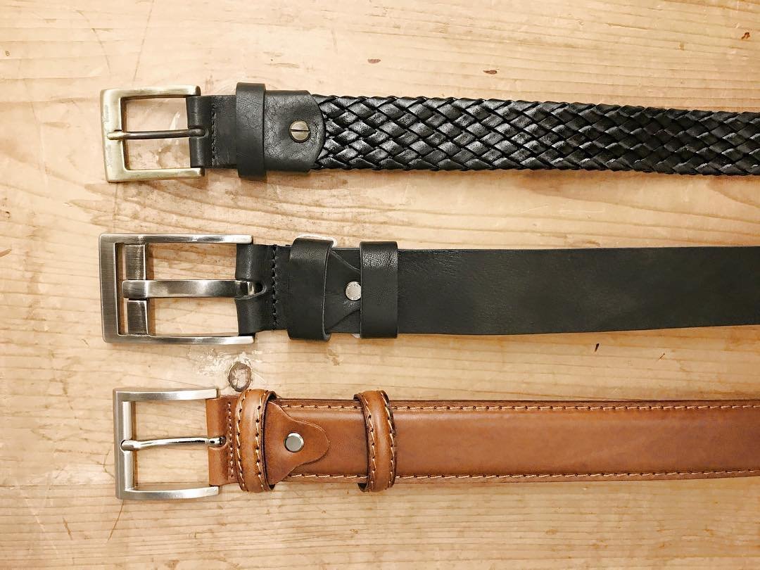 Three leather belts of different styles and colors laid out horizontally on a wooden surface.