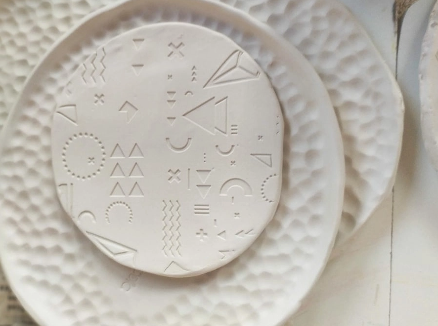 Close-up of a handmade round ceramic plate with geometric embossed patterns on a textured white dish, stacked on a similar dish.