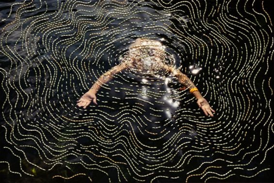 Person floating in a lake with yellow and white embroidery around it.