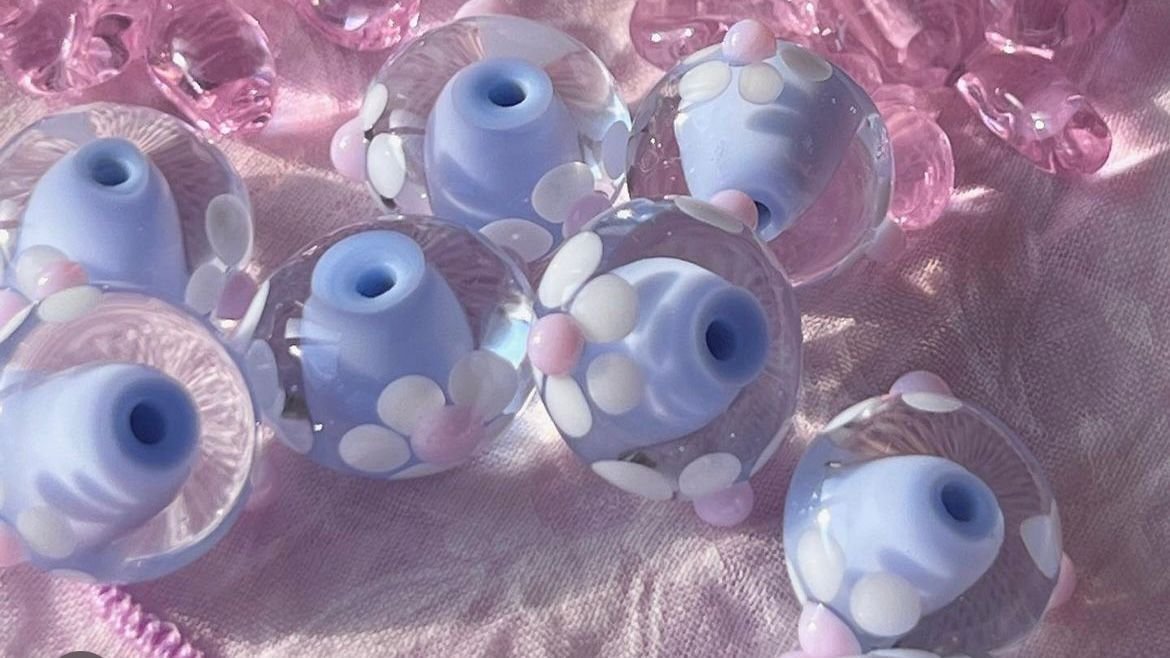 Several decorative glass beads with pastel colors and floral patterns, placed on pink fabric.