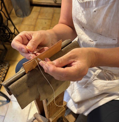 Hands sewing leather while wearing an apron, leather held securely in a stitching pony device.