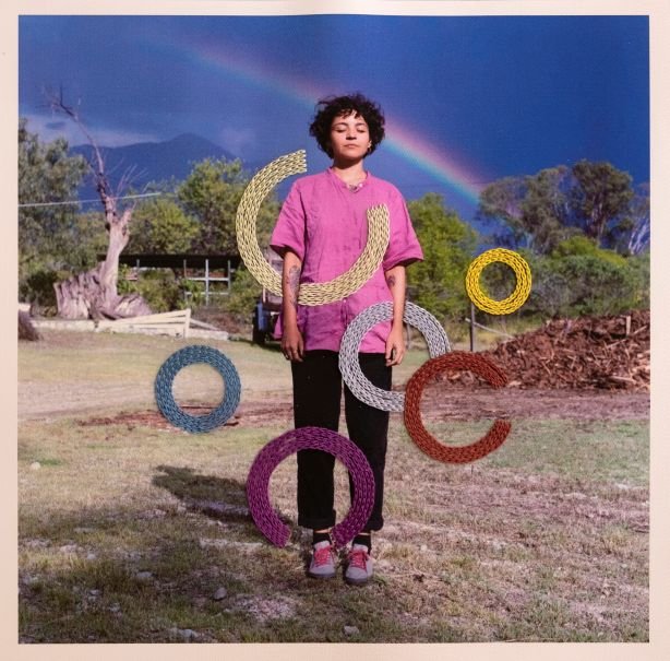 Portrait of the artist standing outdoors with a rainbow in the background, featuring embroidered circular thread designs overlaying the photograph