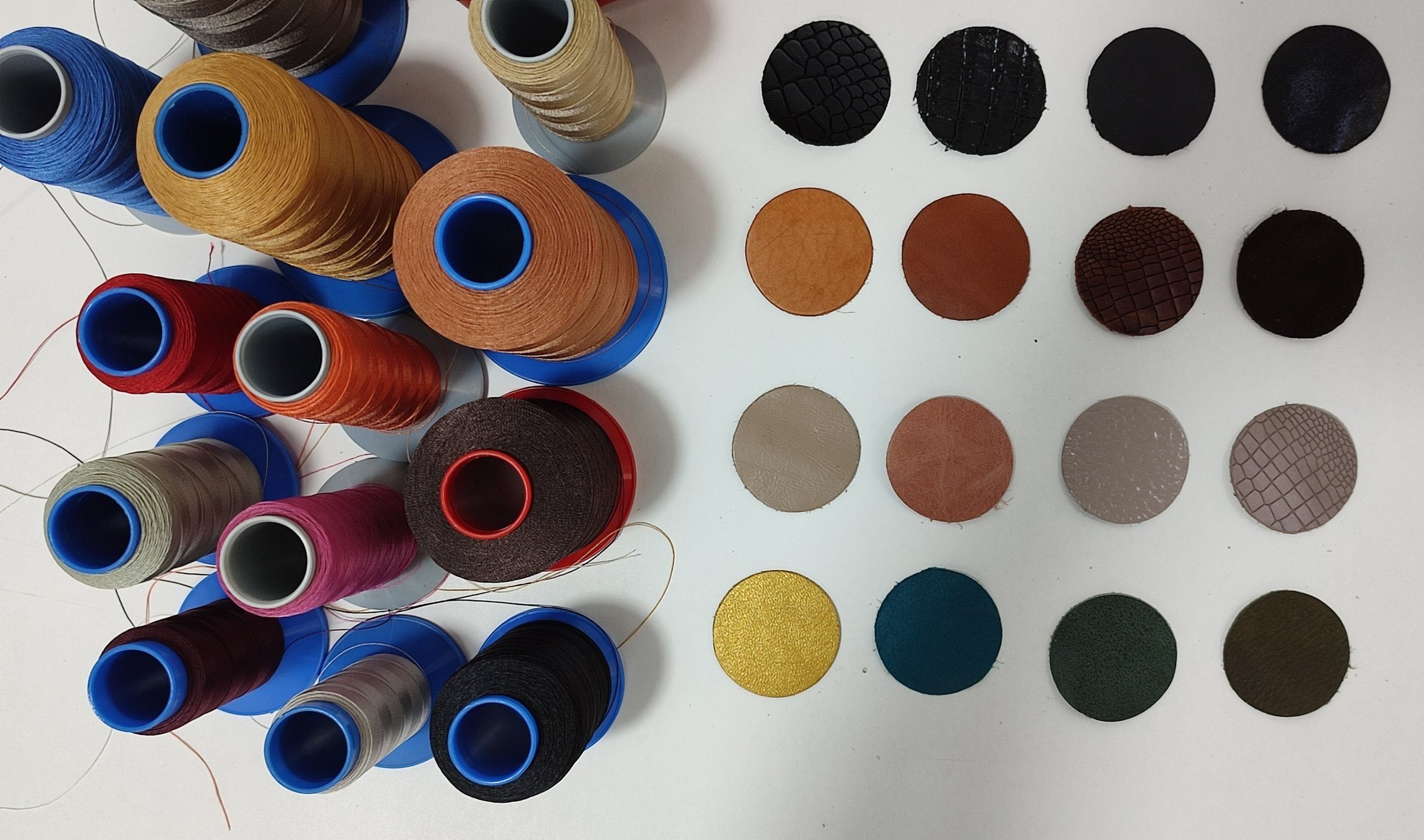 Various spools of colorful thread on a white surface with a color chart of leather swatches and patterns to the right.