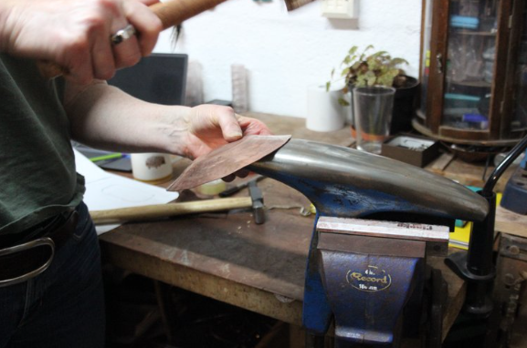 Participant hammering copper bowl in silversmithing workshop