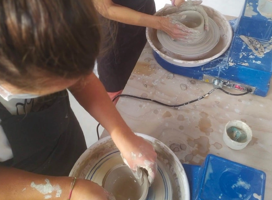 Two people are making pottery on pottery wheels with clay, working hands-on to shape the clay.