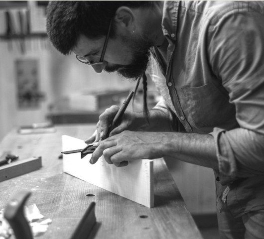 Man measuring a piece of wood with a square and pencil in a woodworking workshop
