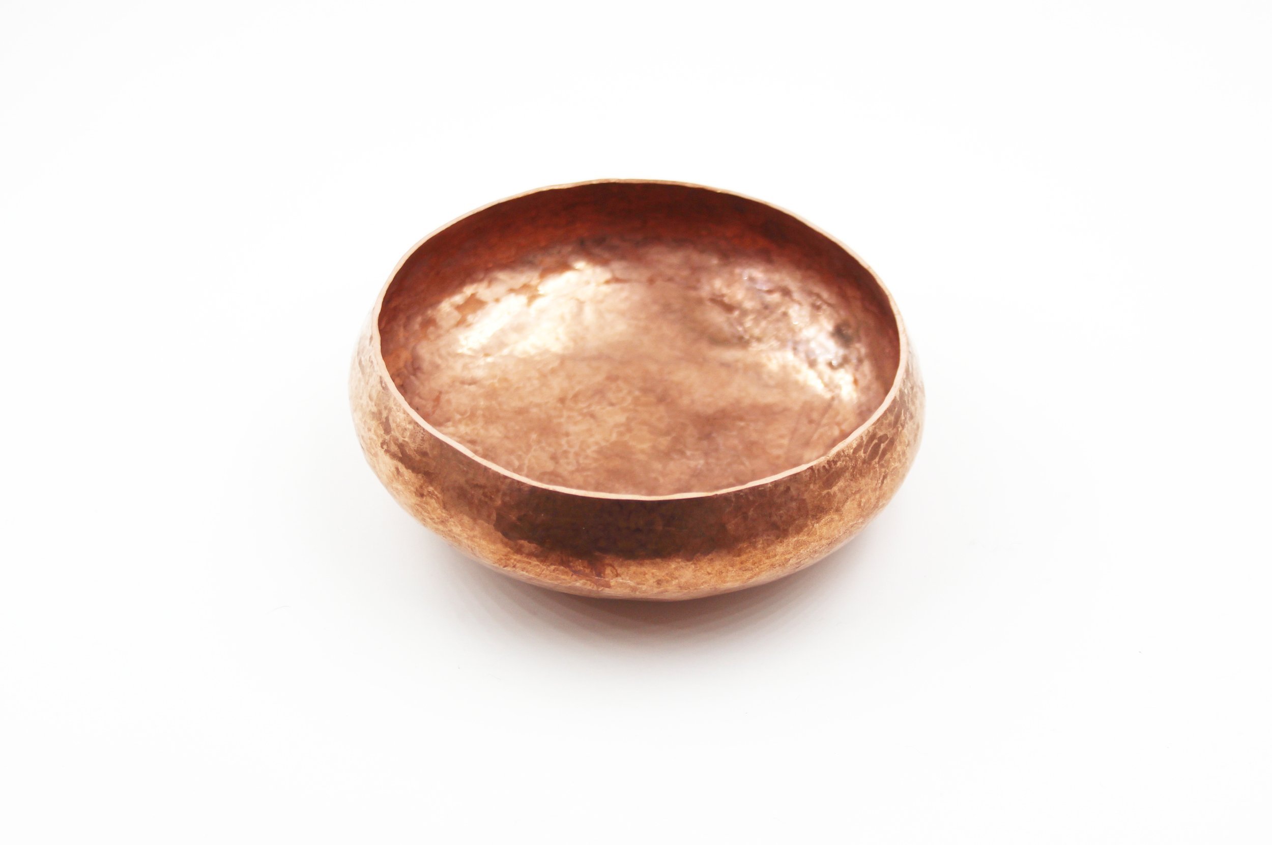 A handmade Round copper bowl with a hammered texture, on a white background.