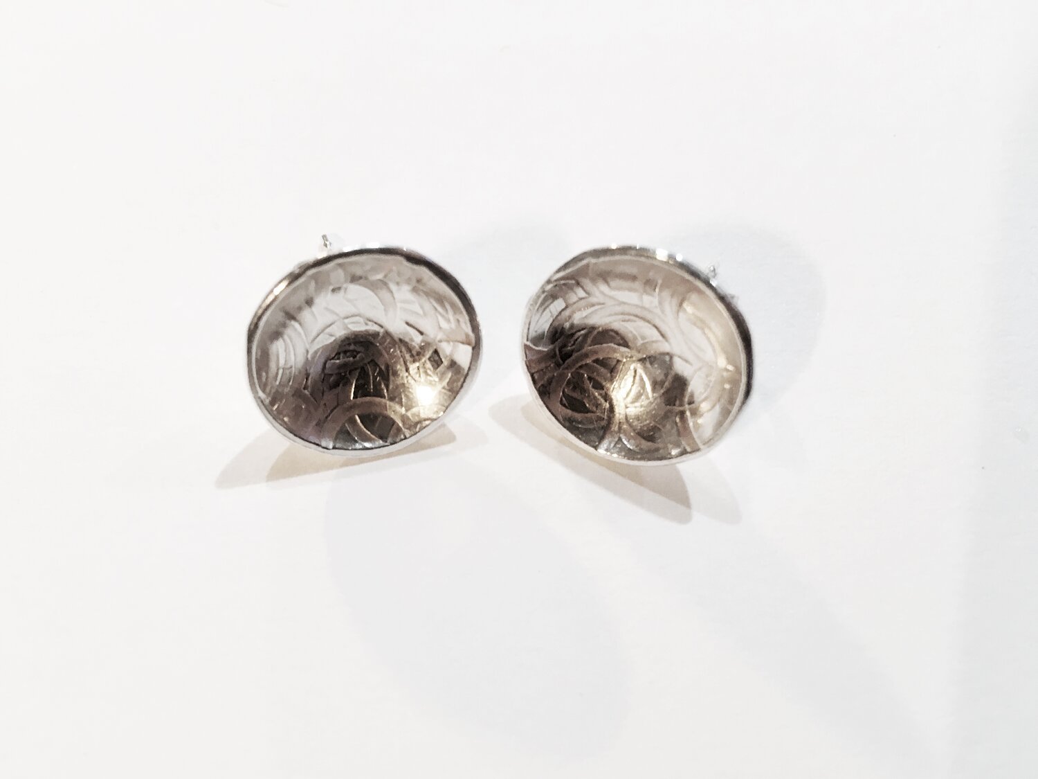 Pair of silver cufflinks with intricate engravings, viewed from the front on a white surface.
