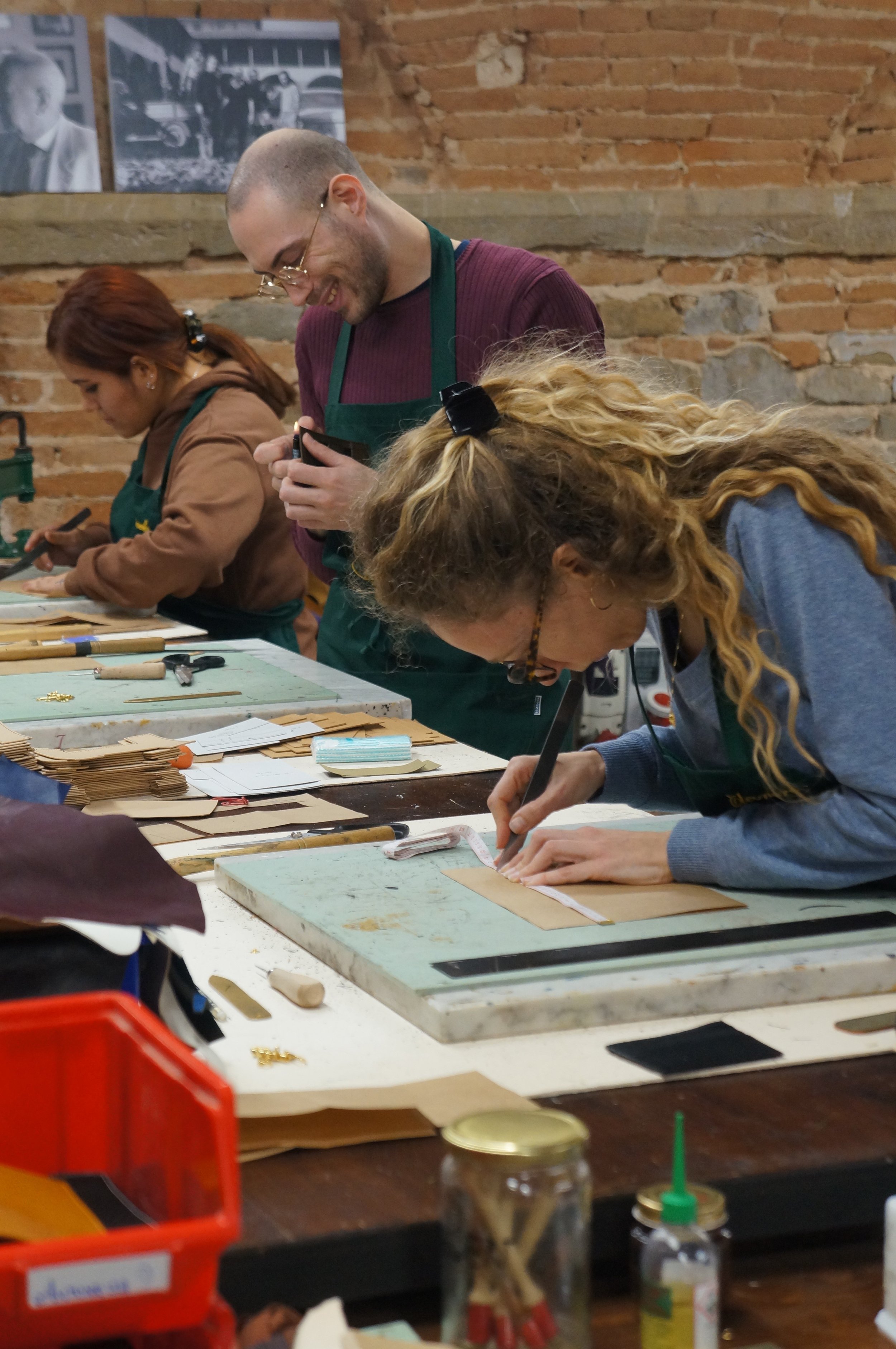 People working on leather craft projects at a craft workshop with tools and supplies on the table.