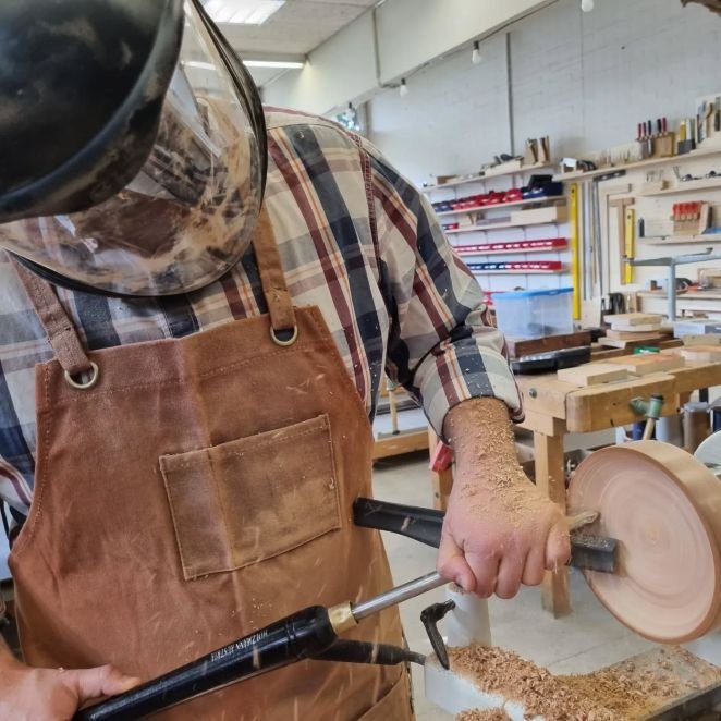 Woodturning student wearing protective helmet while shaping wood on a lathe in a Swiss workshop