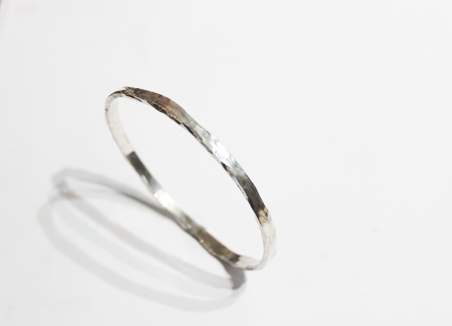A silver textured ring casting a shadow on a white background.