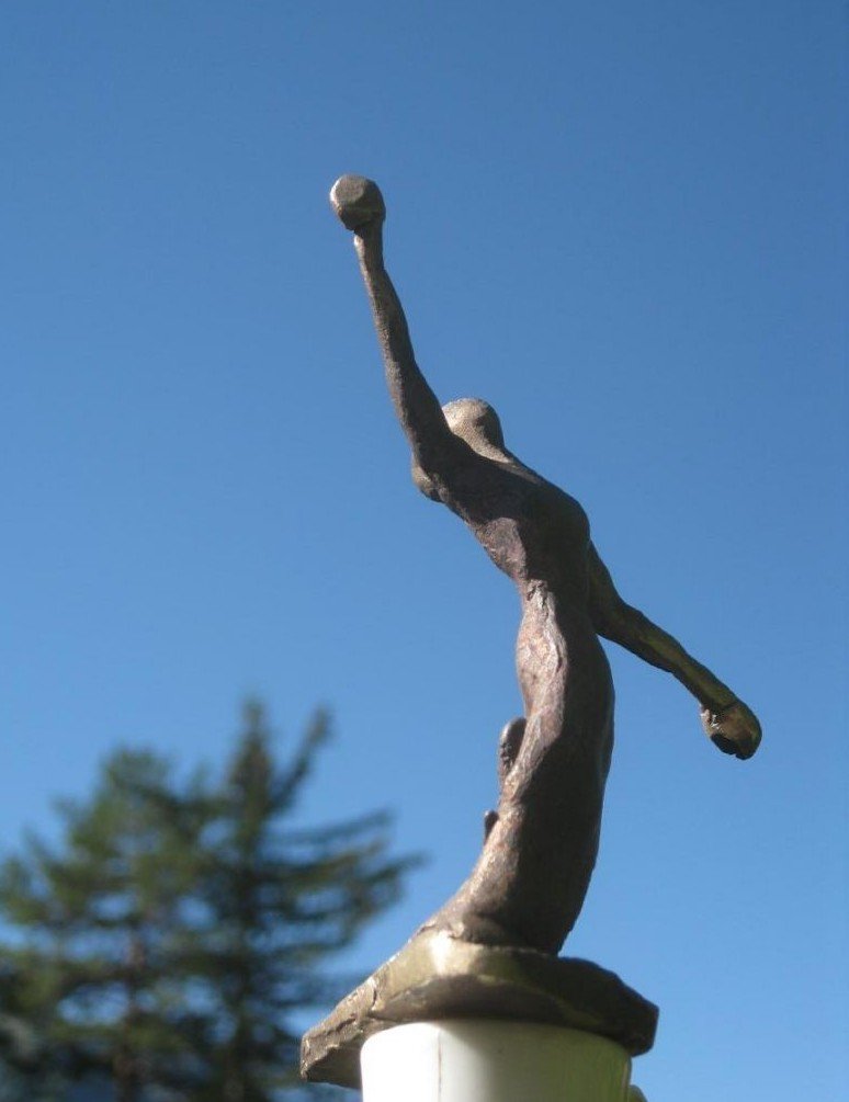 Handmade bronze sculpture of a figure standing with its arms out against a blue sky.
