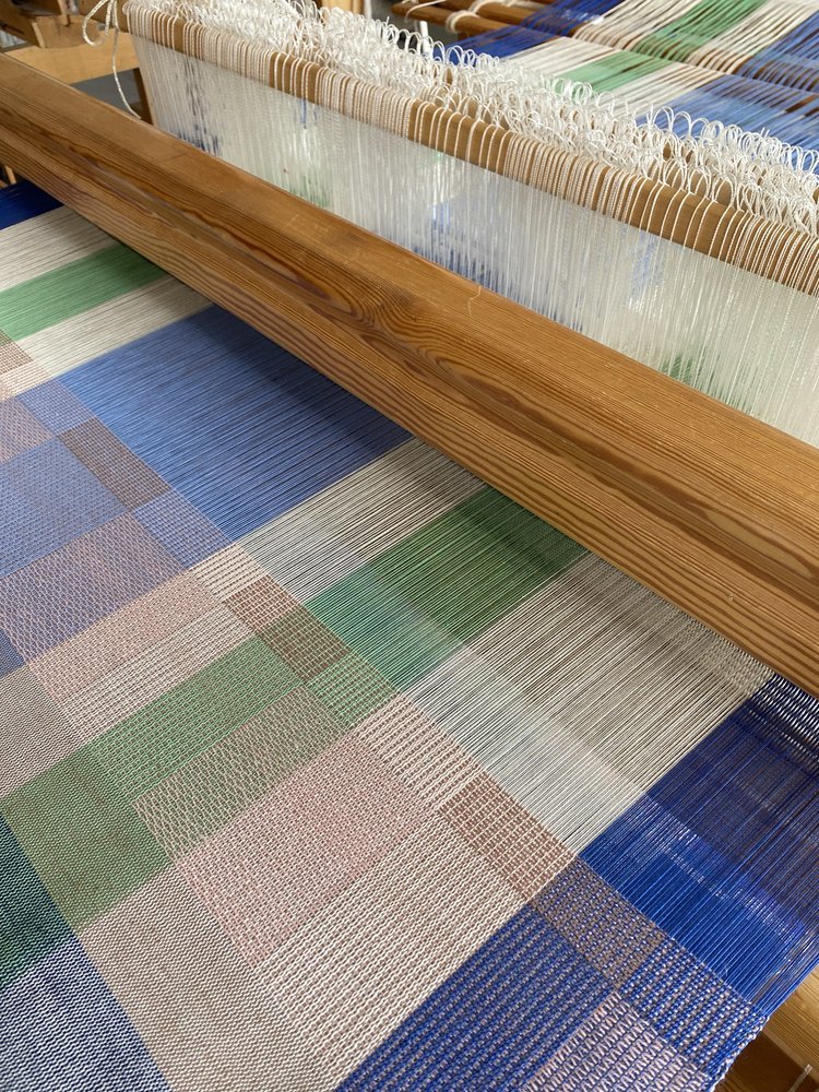 Weaving loom with colorful woven fabric on the table and threads in the background.